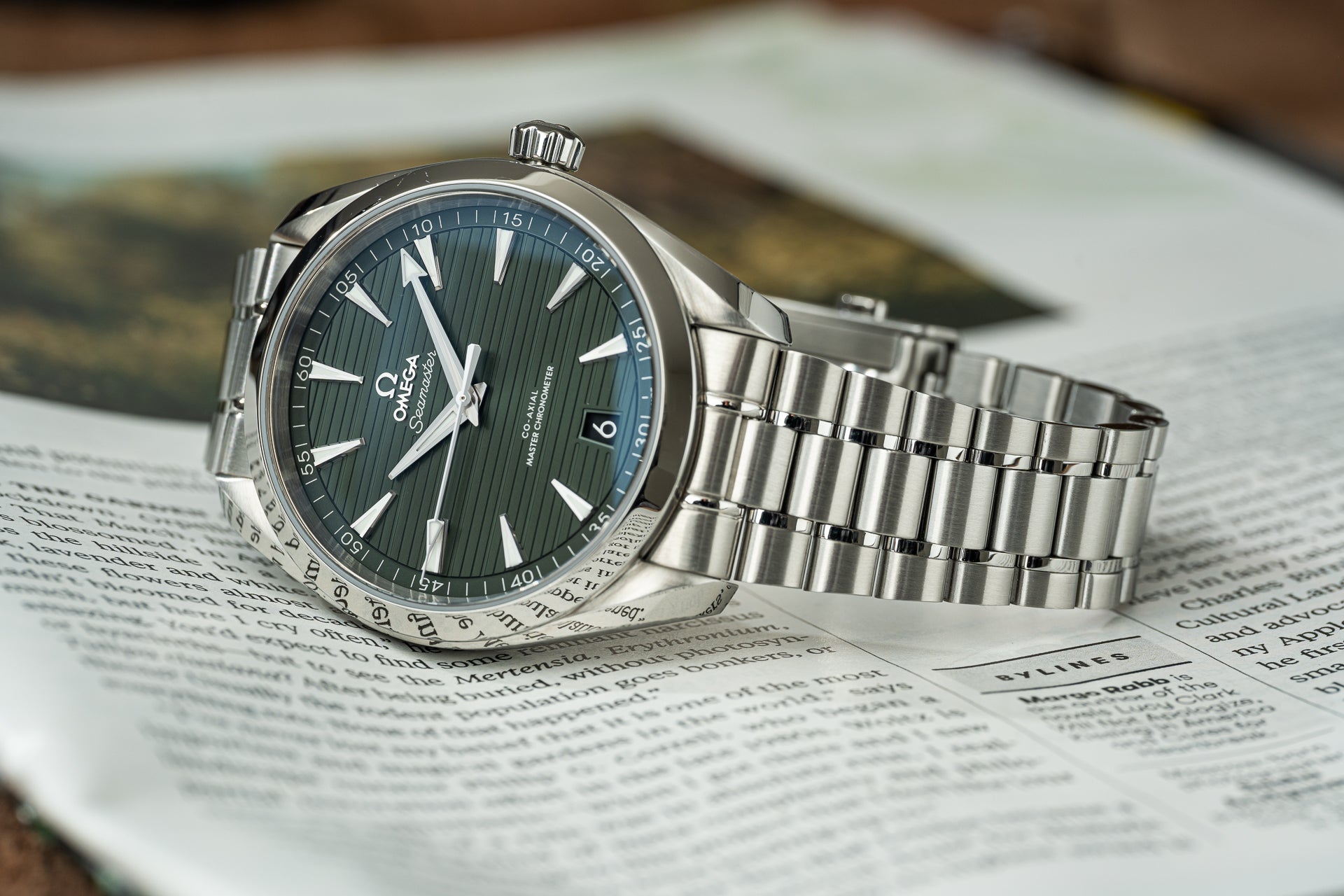Omega Seamaster Aqua Terra 41mm stainless steel watch with green dial on matching bracelet, displayed on newspaper