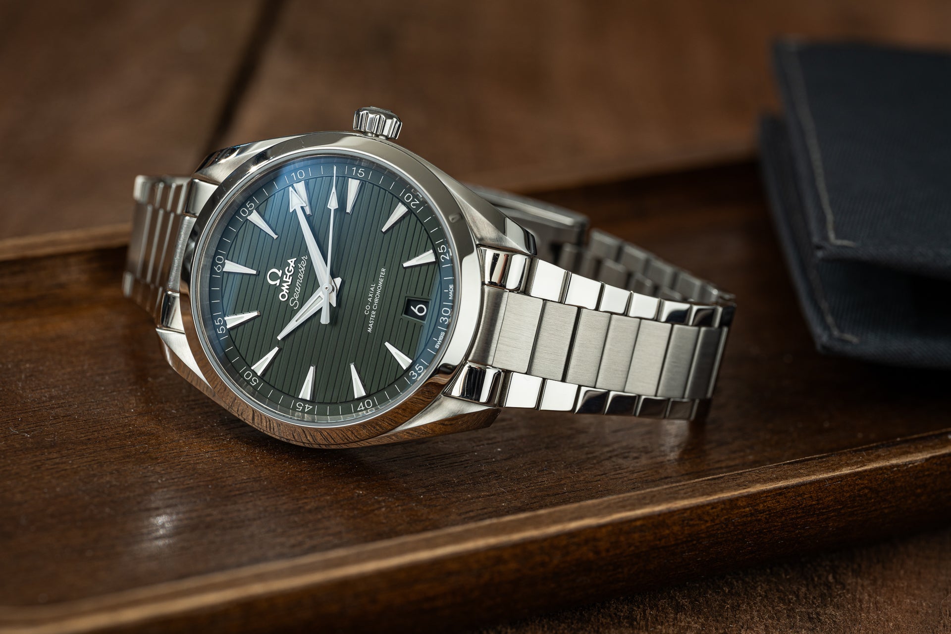 Omega Aqua Terra luxury watch with dark dial and stainless steel flat link bracelet displayed on wooden surface