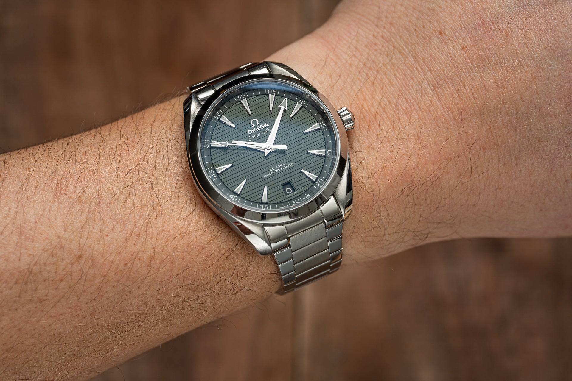 Omega Aqua Terra stainless steel watch with green dial and flat link bracelet worn on wrist