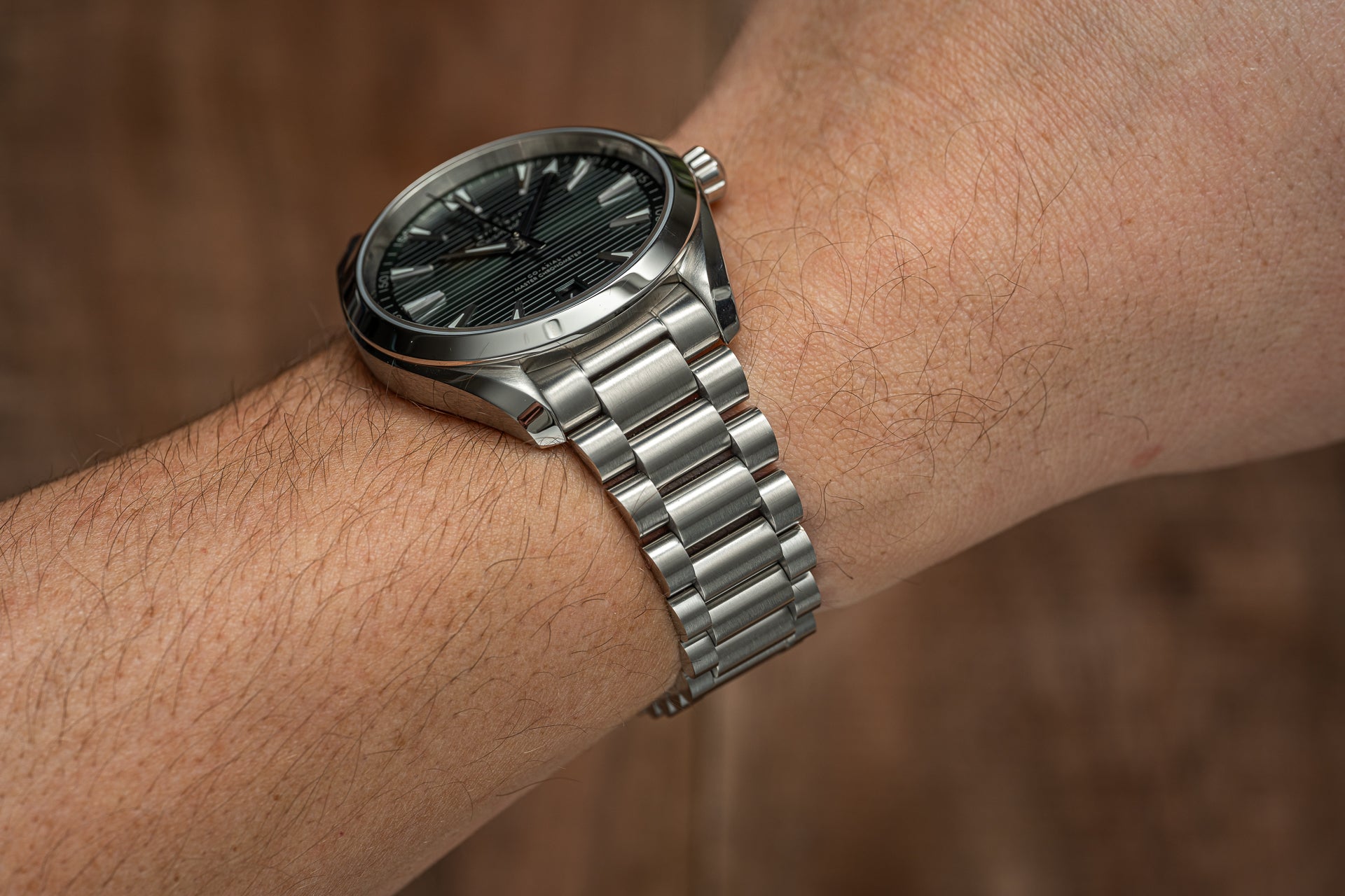 Stainless steel men's watch with black dial on metal bracelet, worn on wrist against neutral background