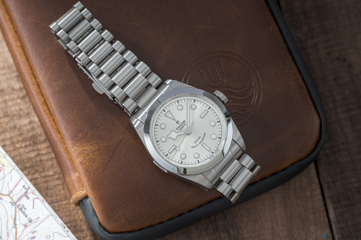 Stainless steel bracelet watch with white dial and integrated metal band on brown leather background