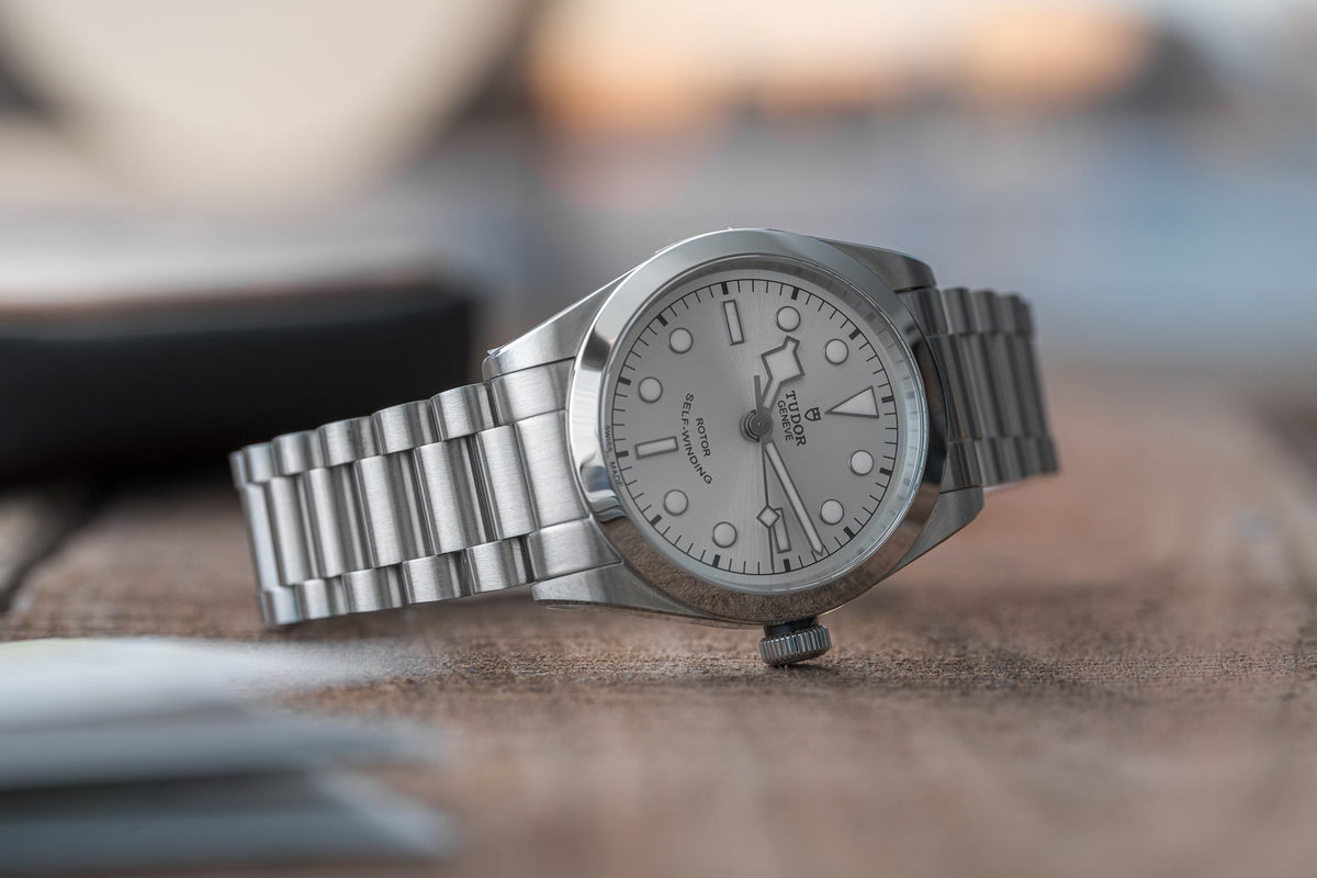 Stainless steel bracelet watch with white dial and hour markers displayed on sandy surface