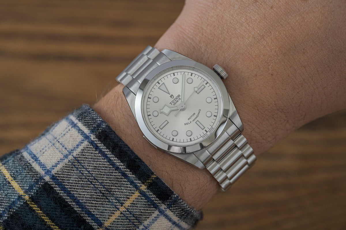 Stainless steel bracelet watch with white dial and self-winding movement worn on wrist with plaid sleeve