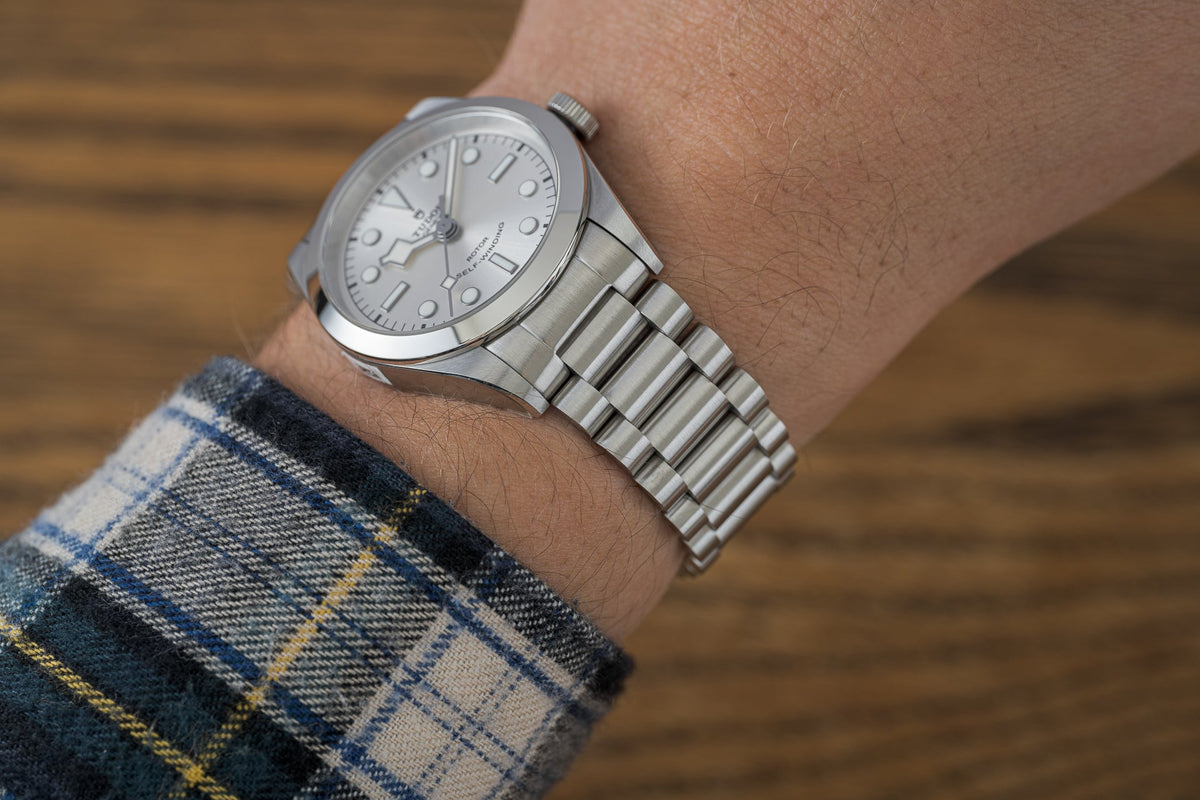 Silver stainless steel watch bracelet with solid links worn on wrist over plaid shirt, showcasing polished and brushed finish