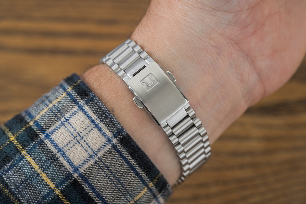 Silver stainless steel bracelet with solid end links on male wrist wearing plaid shirt, wooden background