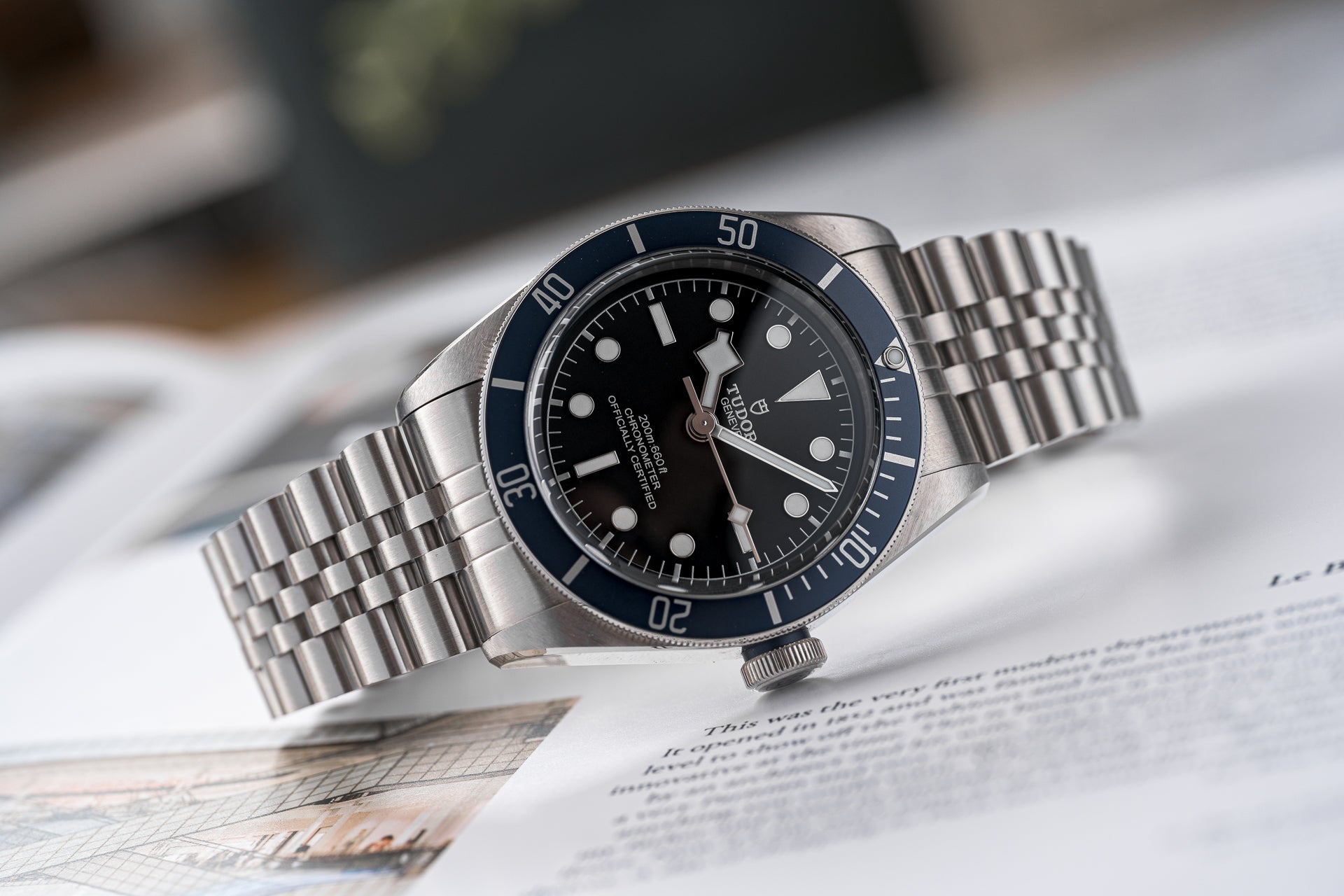 Stainless steel dive watch with black dial, blue bezel, and matching metal bracelet on document background
