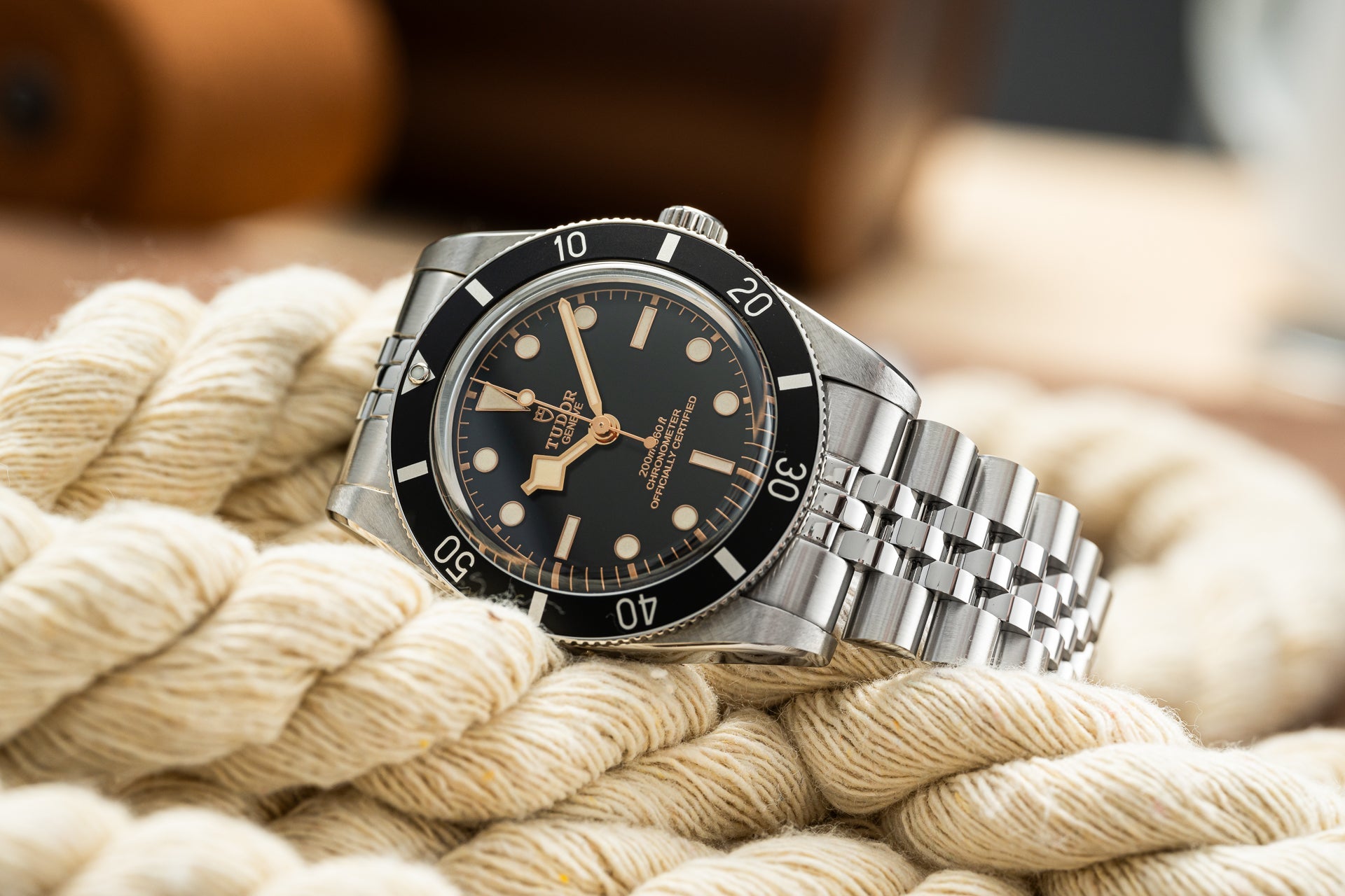 Vintage-style Tudor dive watch with black dial, rose gold hands, and rotating bezel on steel bracelet, displayed on nautical rope
