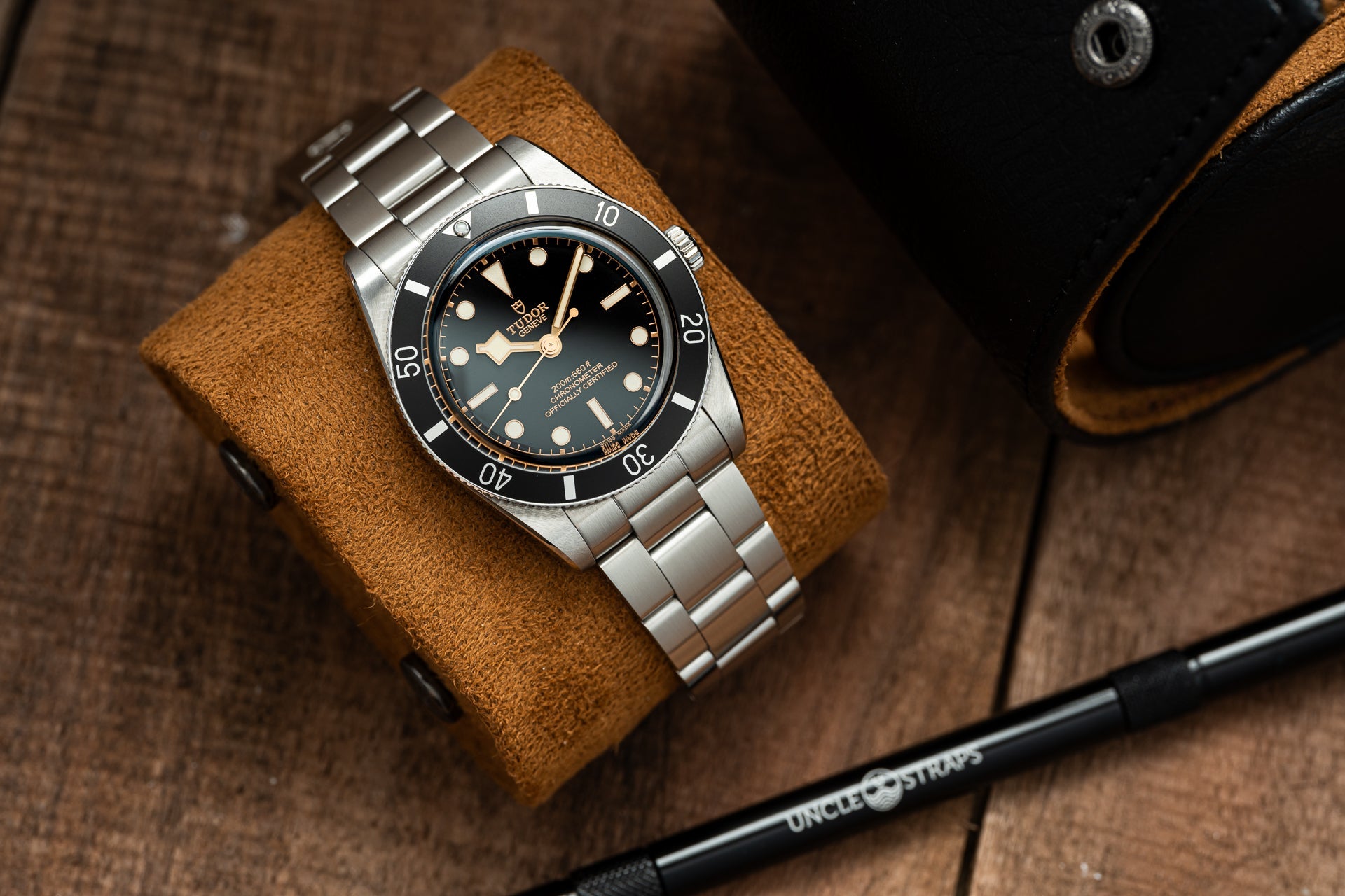 Stainless steel Tudor Black Bay 54 dive watch with black dial on tan leather strap, displayed on wooden surface