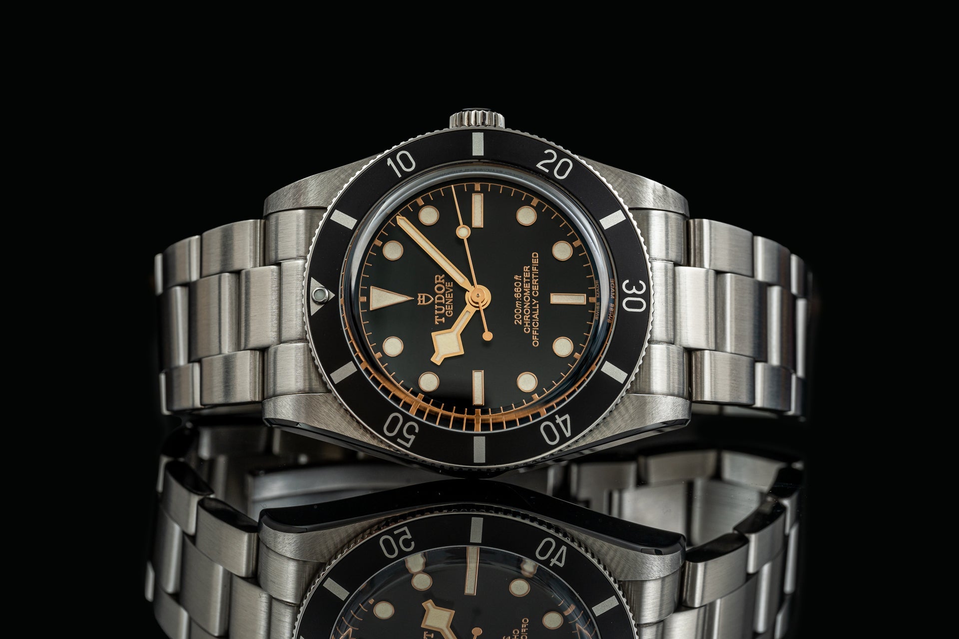 Stainless steel Tudor Black Bay 54 watch with black dial, gold hour markers, rotating bezel, and matching bracelet on black background