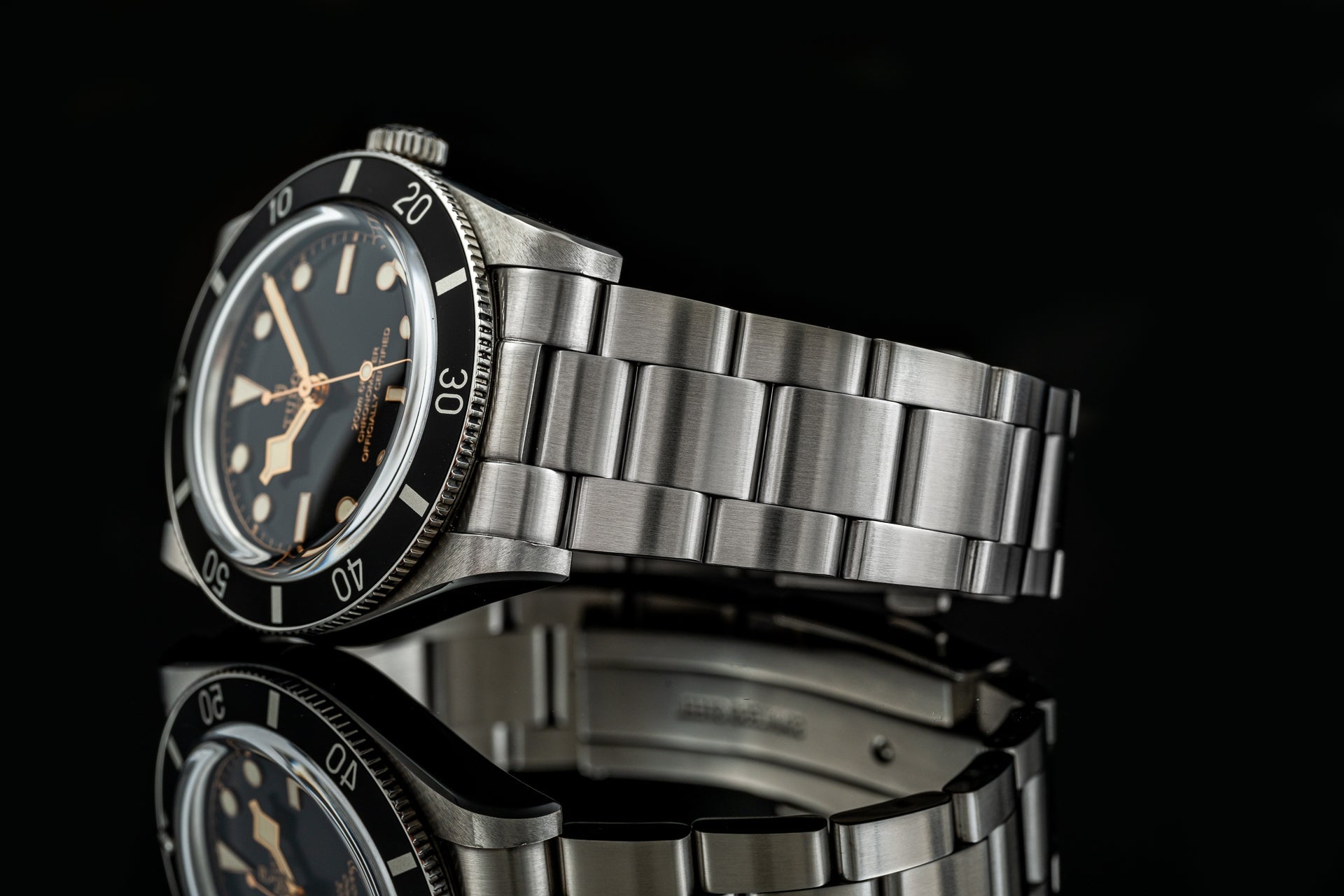 Vintage-style stainless steel dive watch with black dial, rose gold hour markers, rotatable bezel, and matching metal bracelet against black background