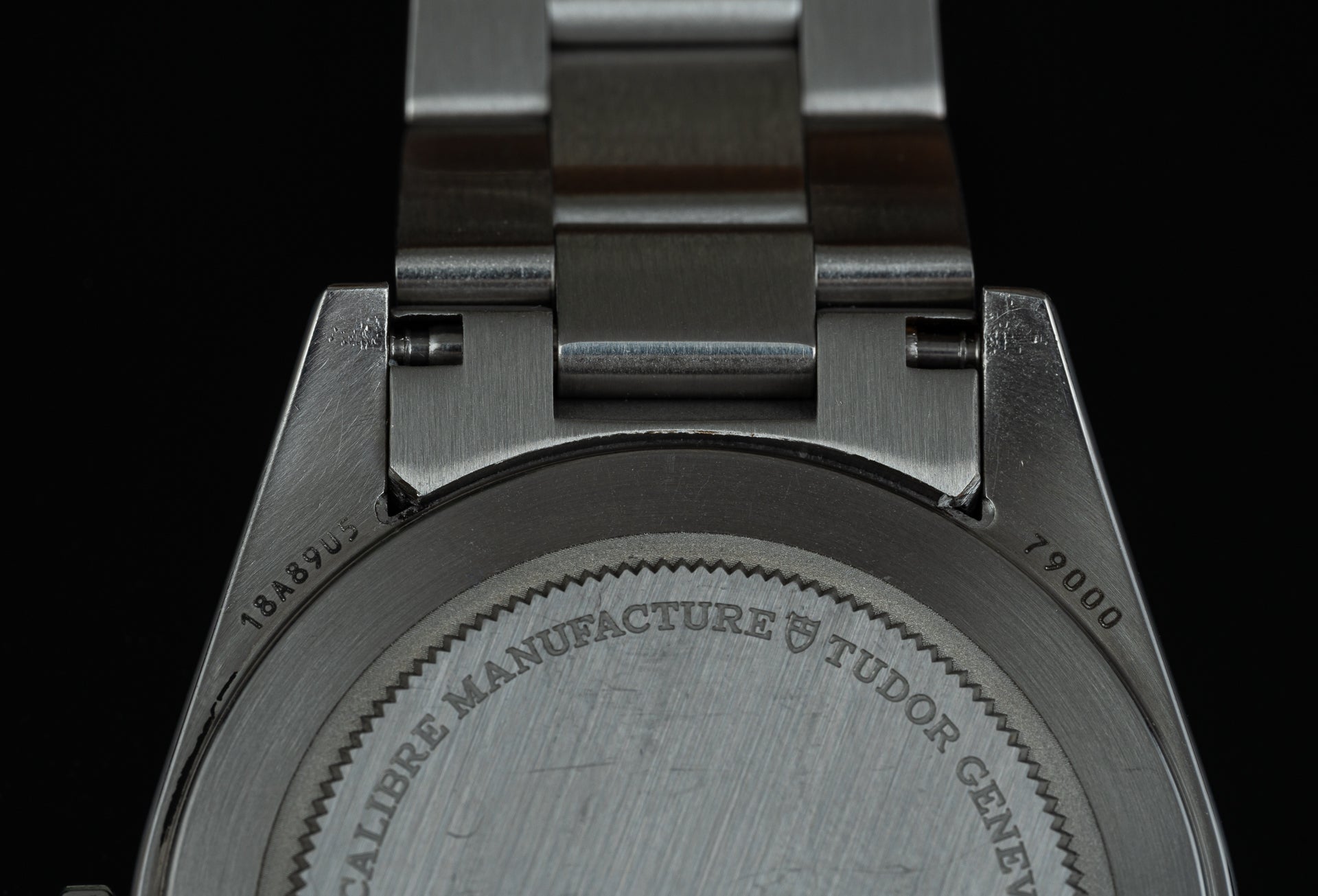 Stainless steel watch bracelet with solid links and Tudor Crown engraved caseback detail, closeup view