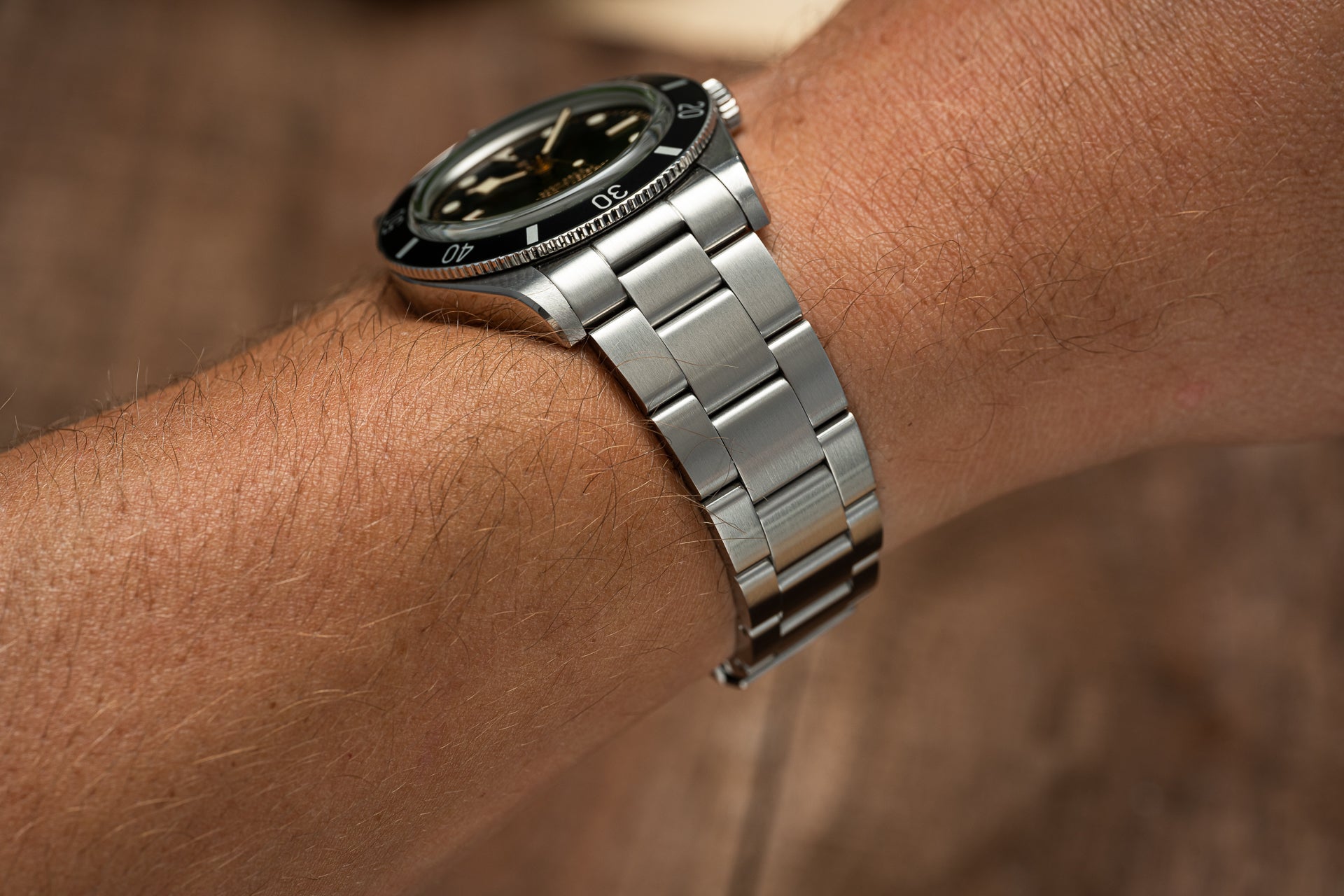 Stainless steel bracelet watch with black dial and rotating bezel worn on wrist
