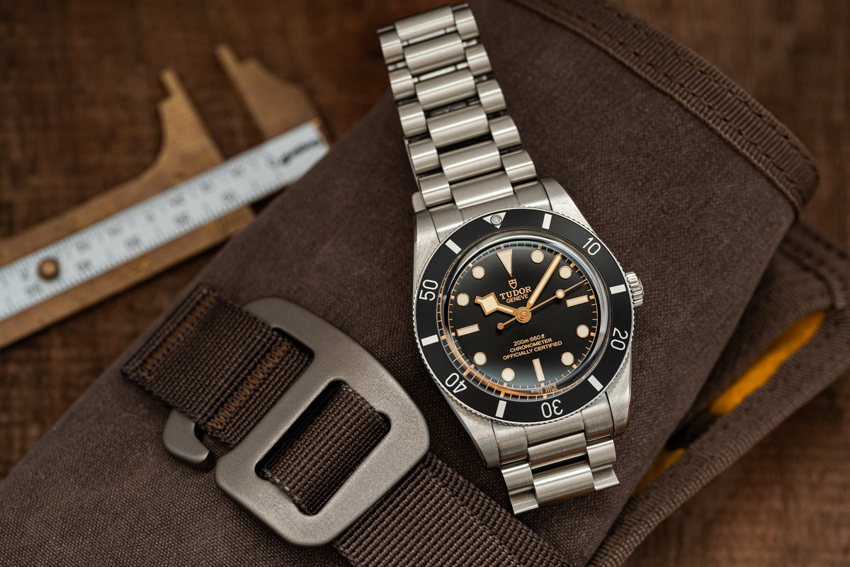 Tudor Black Bay 54 dive watch with stainless steel bracelet and black dial on brown tactical gear background