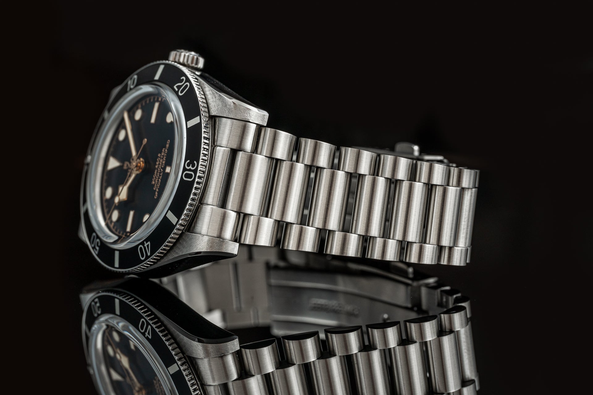 Stainless steel dive watch with black dial and applied indices on brushed metal bracelet against dark background