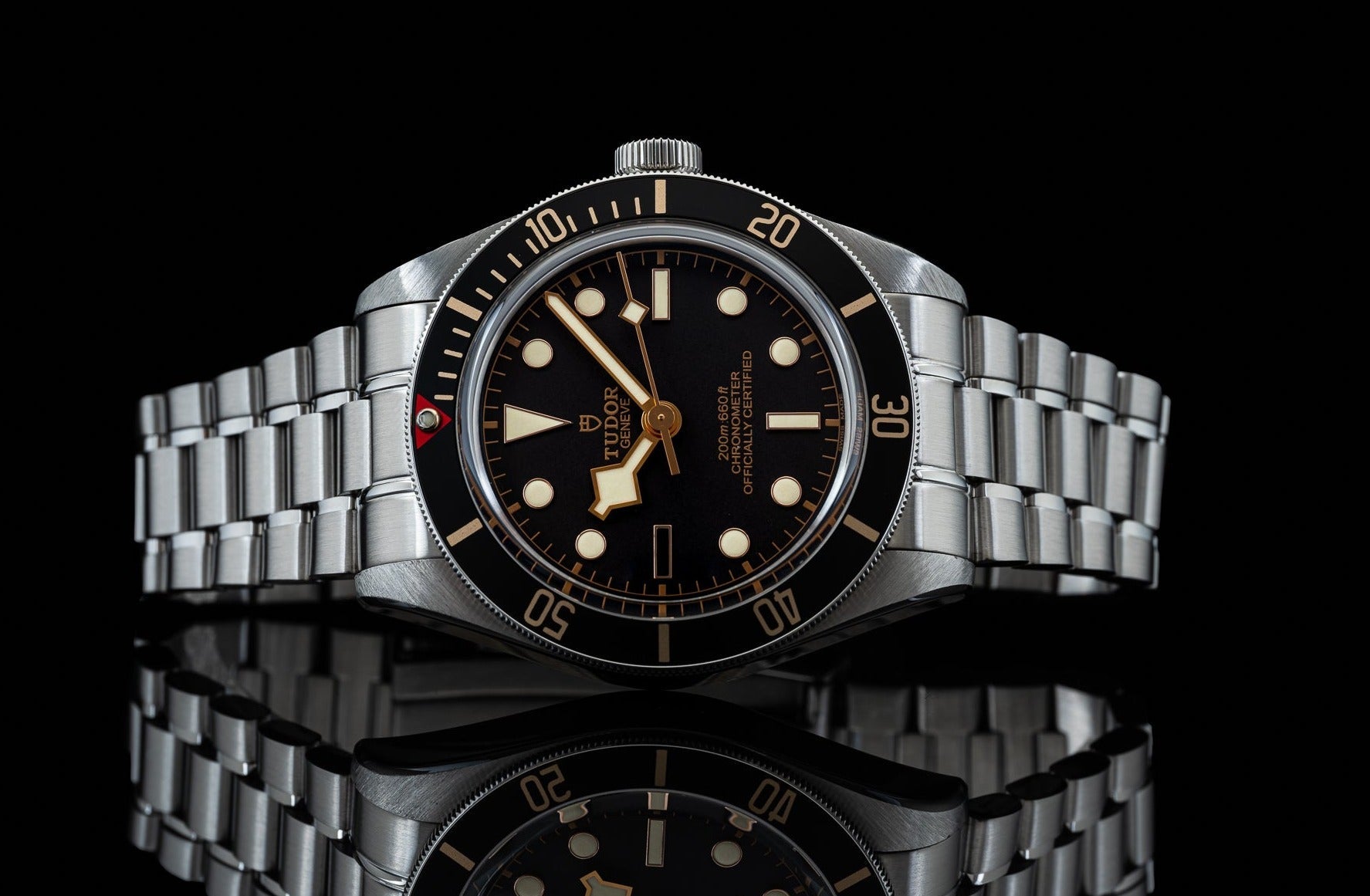Tudor Black Bay 58 watch with stainless steel bracelet, black dial, and gilt indices on reflective surface