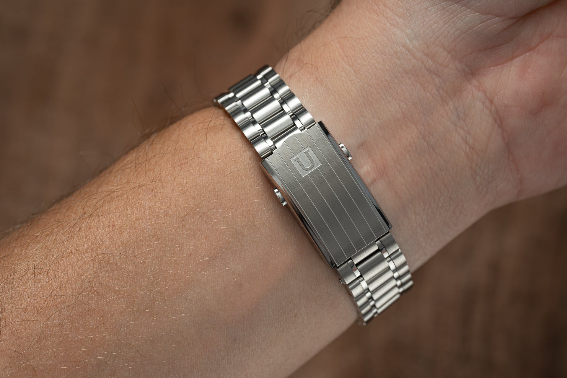 Stainless steel bracelet with polished cylindrical links fitted on wrist, featuring engraved logo on brushed rectangular clasp
