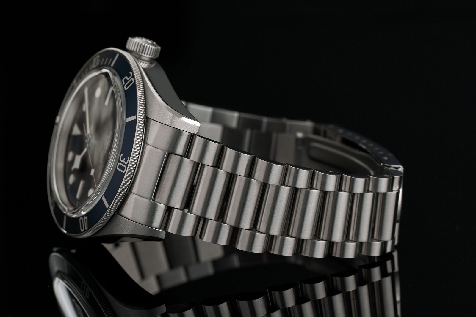Stainless steel bracelet watch with dark blue dial and metal band against black background