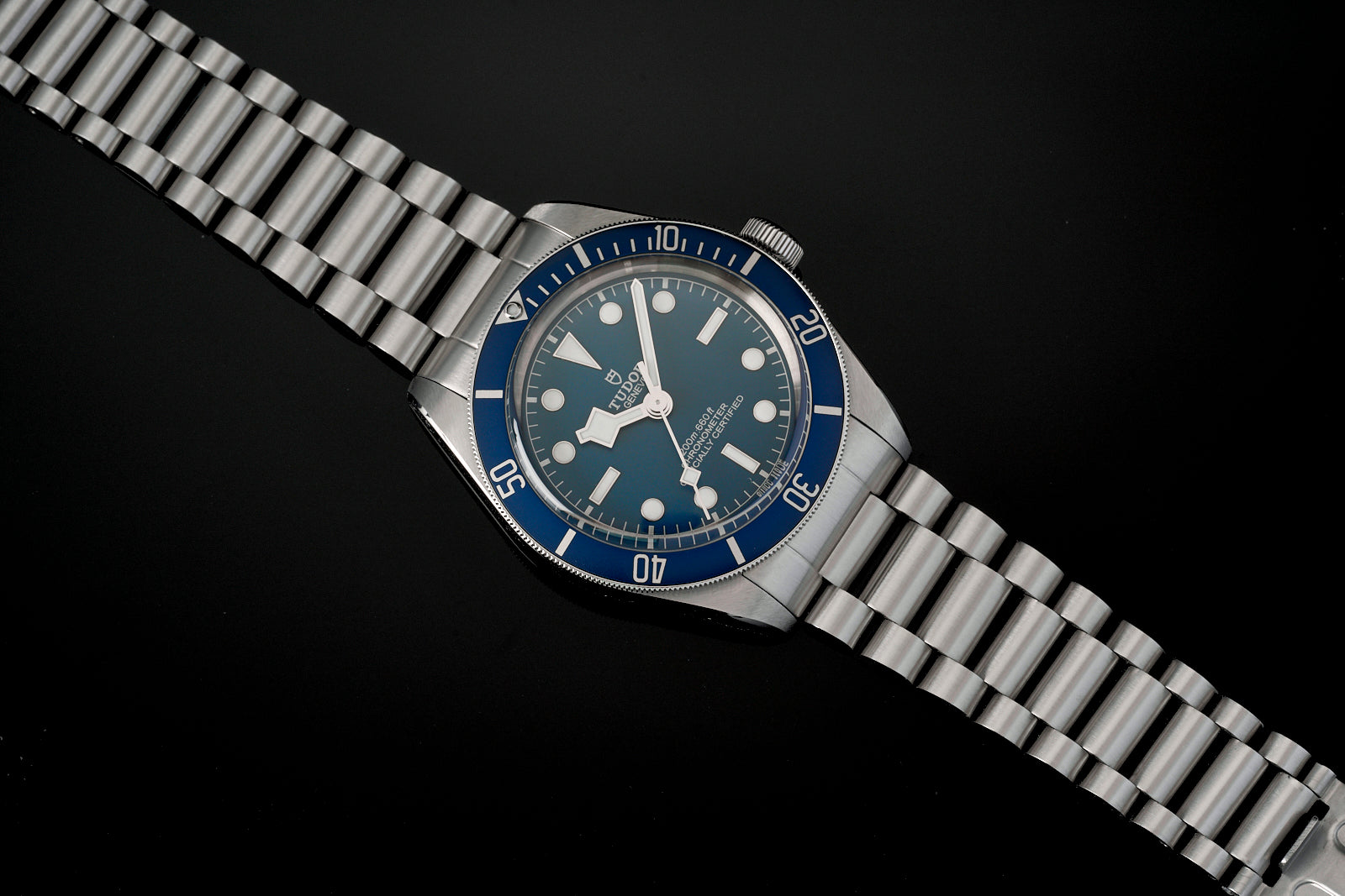 Stainless steel dive watch with blue bezel, dark blue dial, and matching metal bracelet on black background