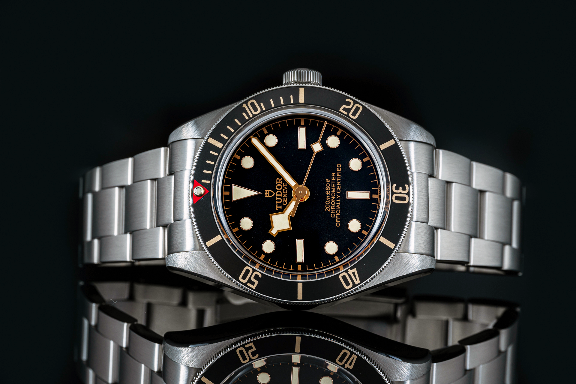 Stainless steel dive watch with black dial, gold hour markers, rotating bezel, and matching metal bracelet on dark background