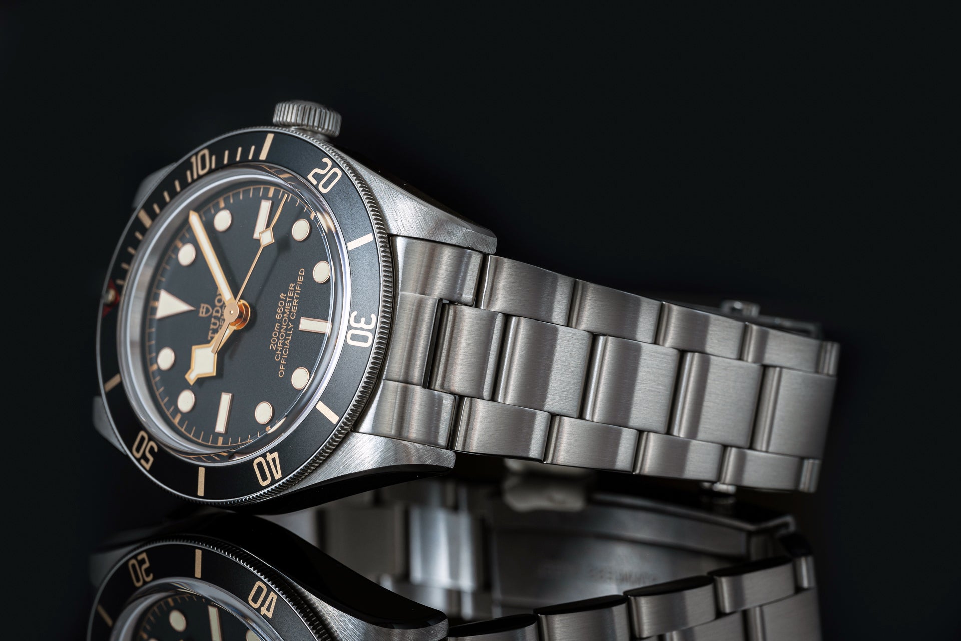 Stainless steel sports watch with black dial, gold hour markers, rotating bezel, and matching metal bracelet on black background