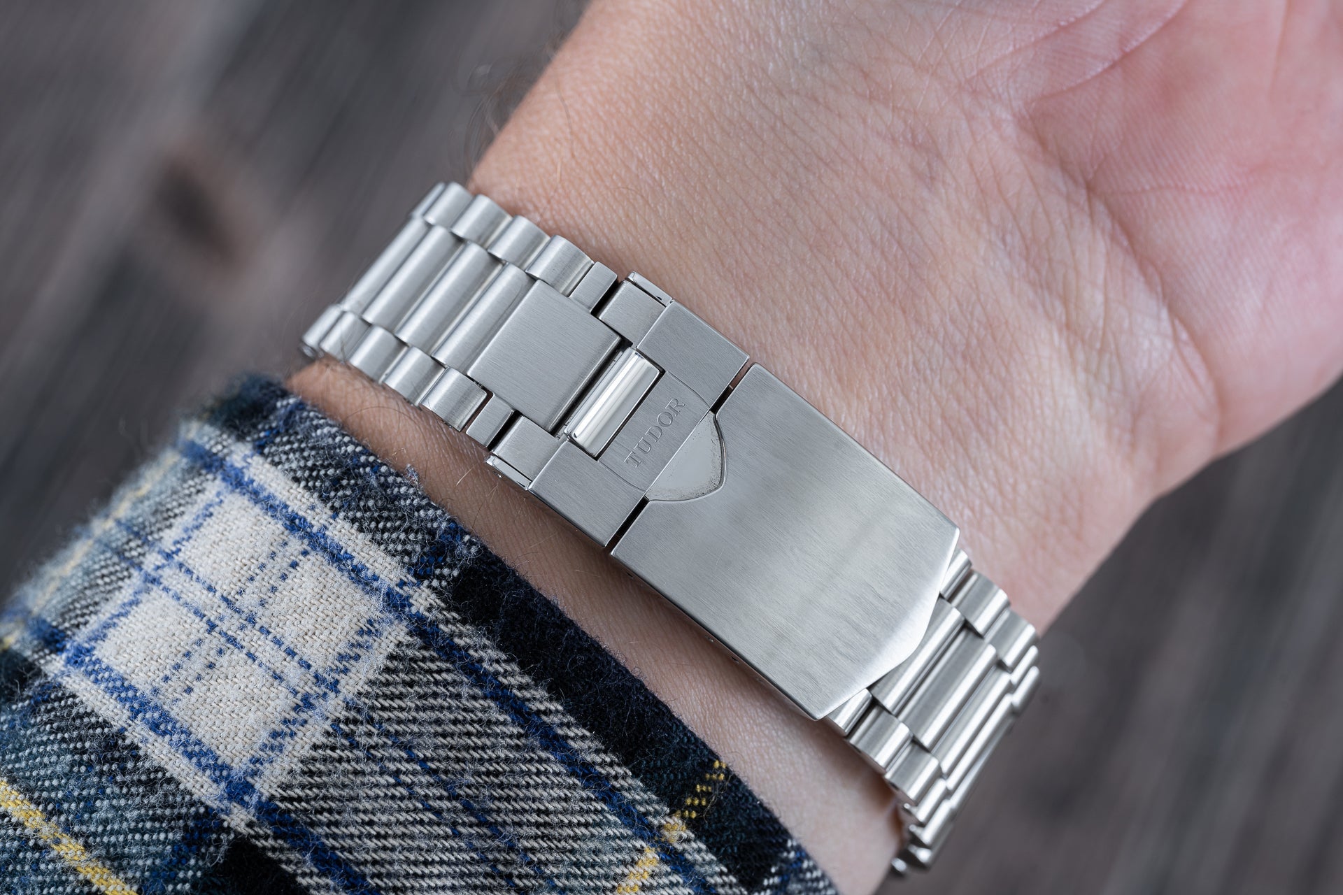 Stainless steel watch bracelet with solid links and folding clasp worn on wrist with plaid shirt cuff