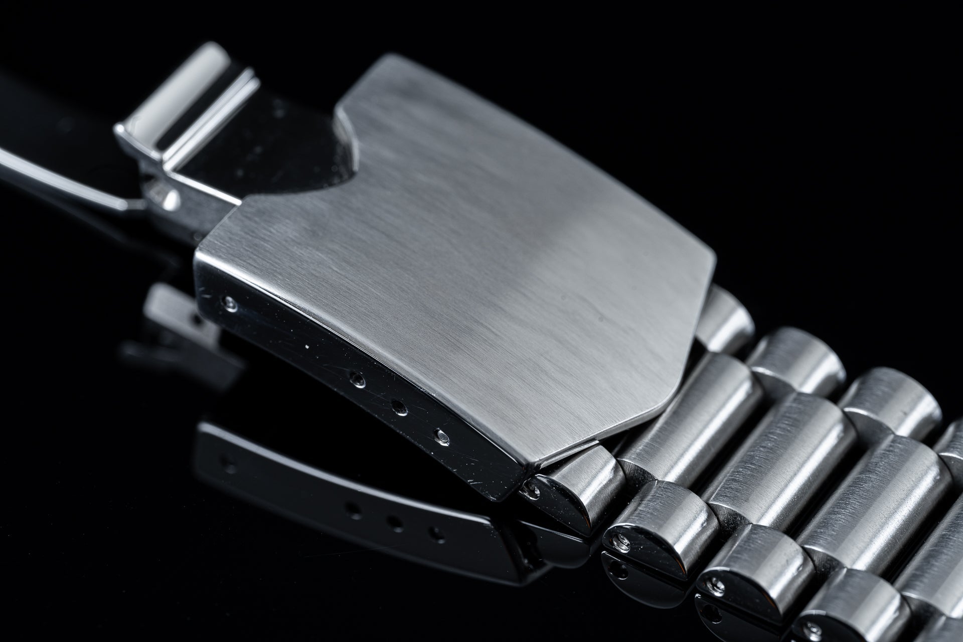 Brushed stainless steel watch bracelet with solid end links and cylindrical center links, angled view on black background