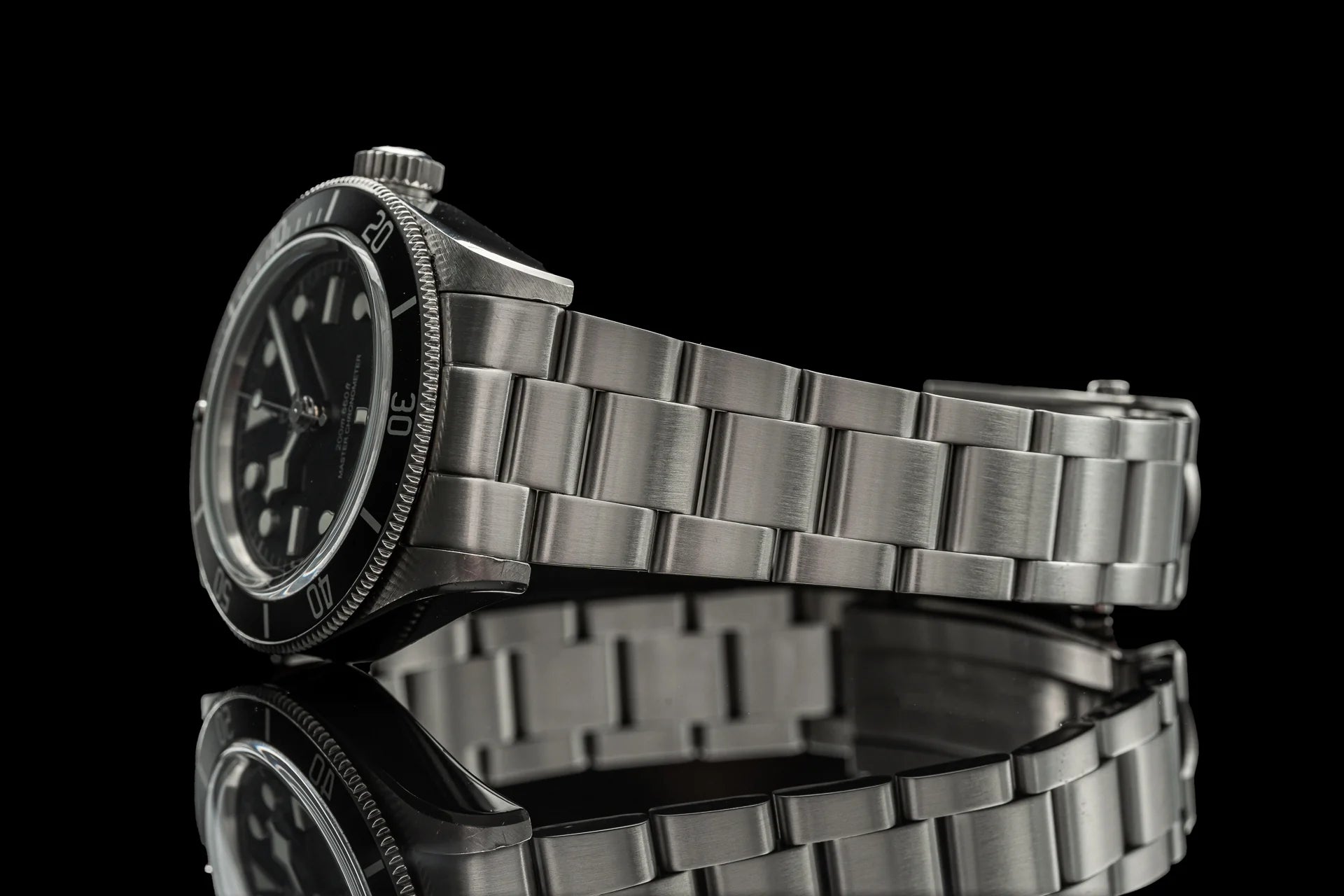 Stainless steel bracelet watch with black dial and rotating bezel on reflective black background
