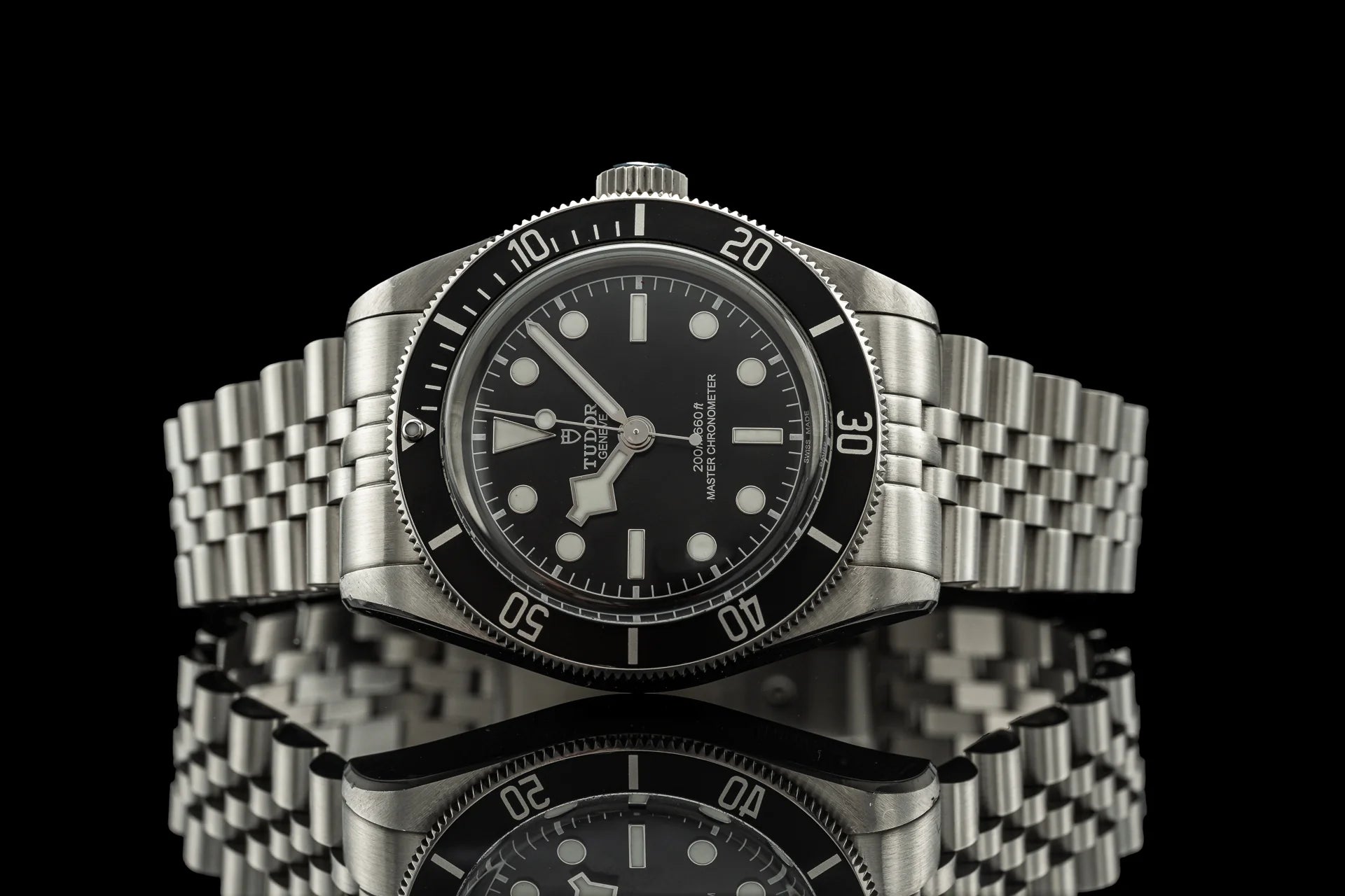 Stainless steel Tudor dive watch with black dial, rotating bezel, and matching metal bracelet on black background