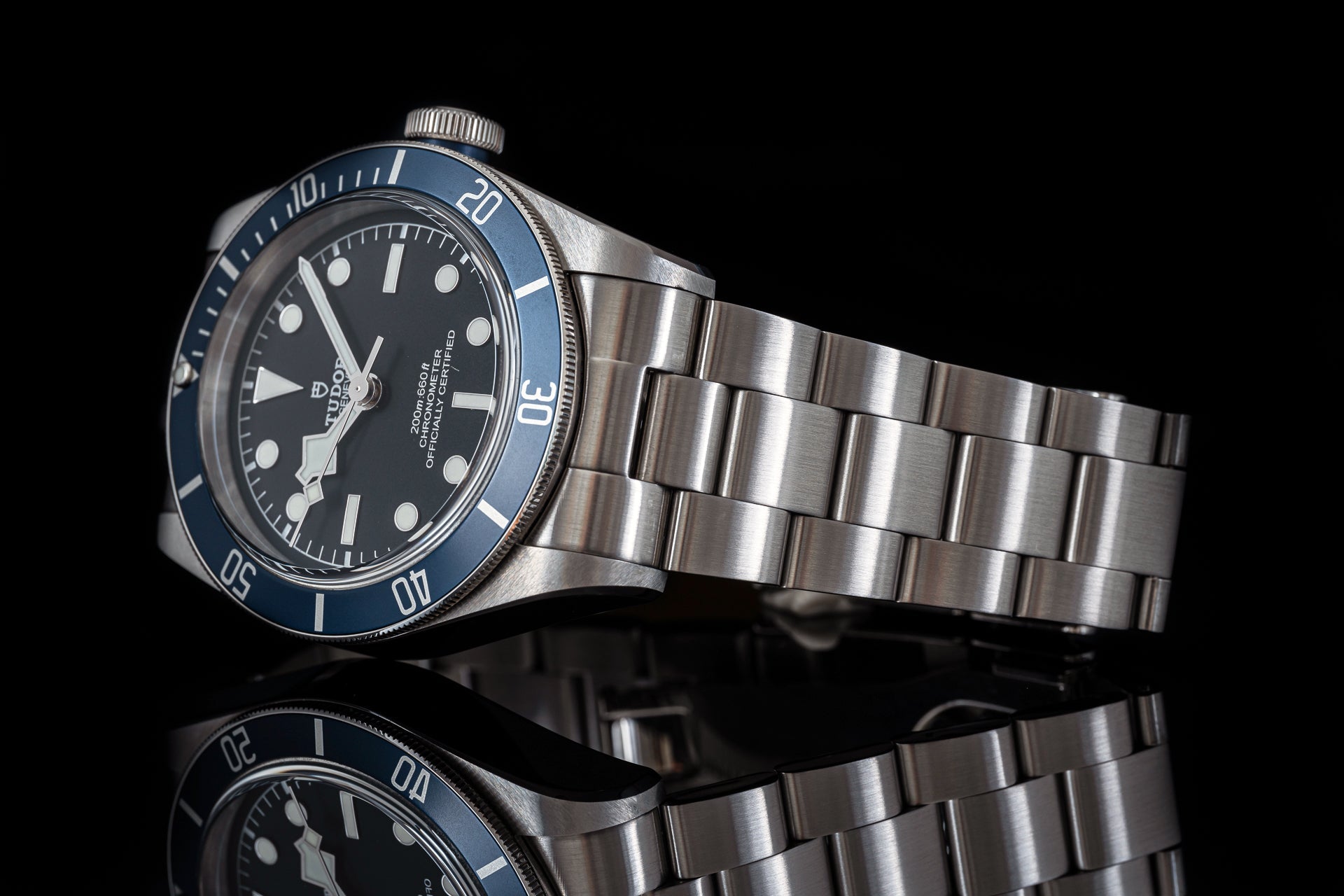 Tudor diving watch with stainless steel bracelet, black dial, blue bezel, white hour markers and hands on black background