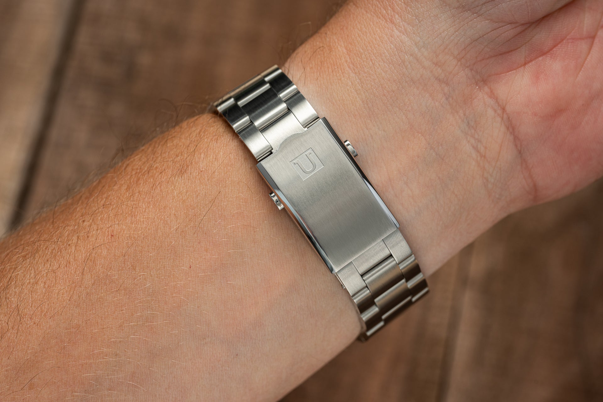 Stainless steel watch bracelet on wrist showing metal links and clasp with engraved logo detail