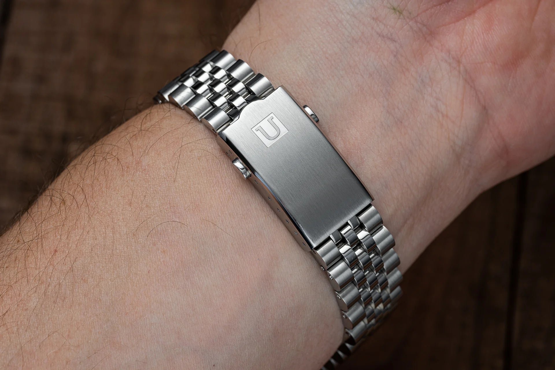 Stainless steel bracelet with polished links and brushed center link worn on wrist with engraved logo clasp