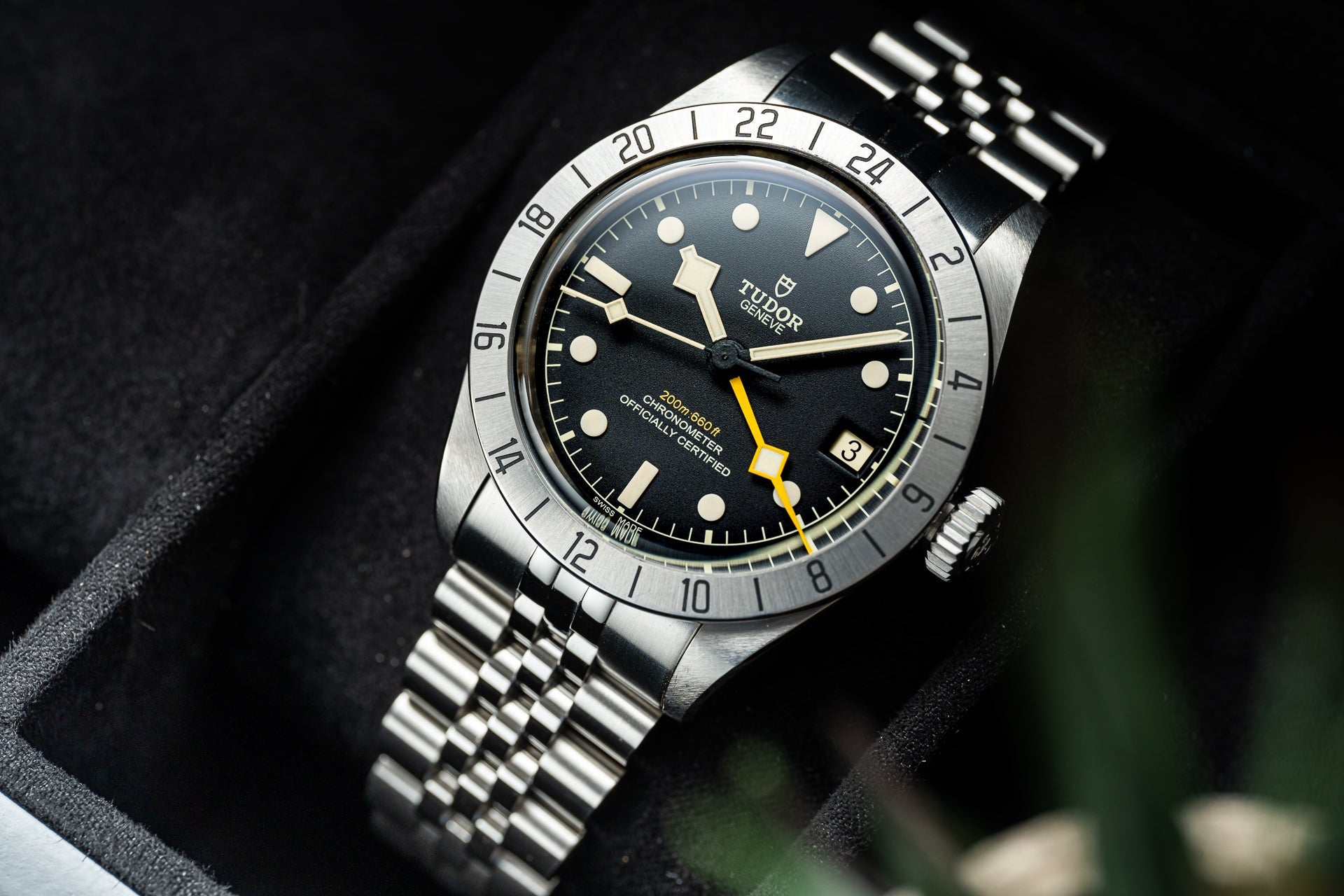 Tudor Black Bay Pro stainless steel watch with black dial, luminous hour markers, yellow hand accent, and steel jubilee bracelet on dark fabric background