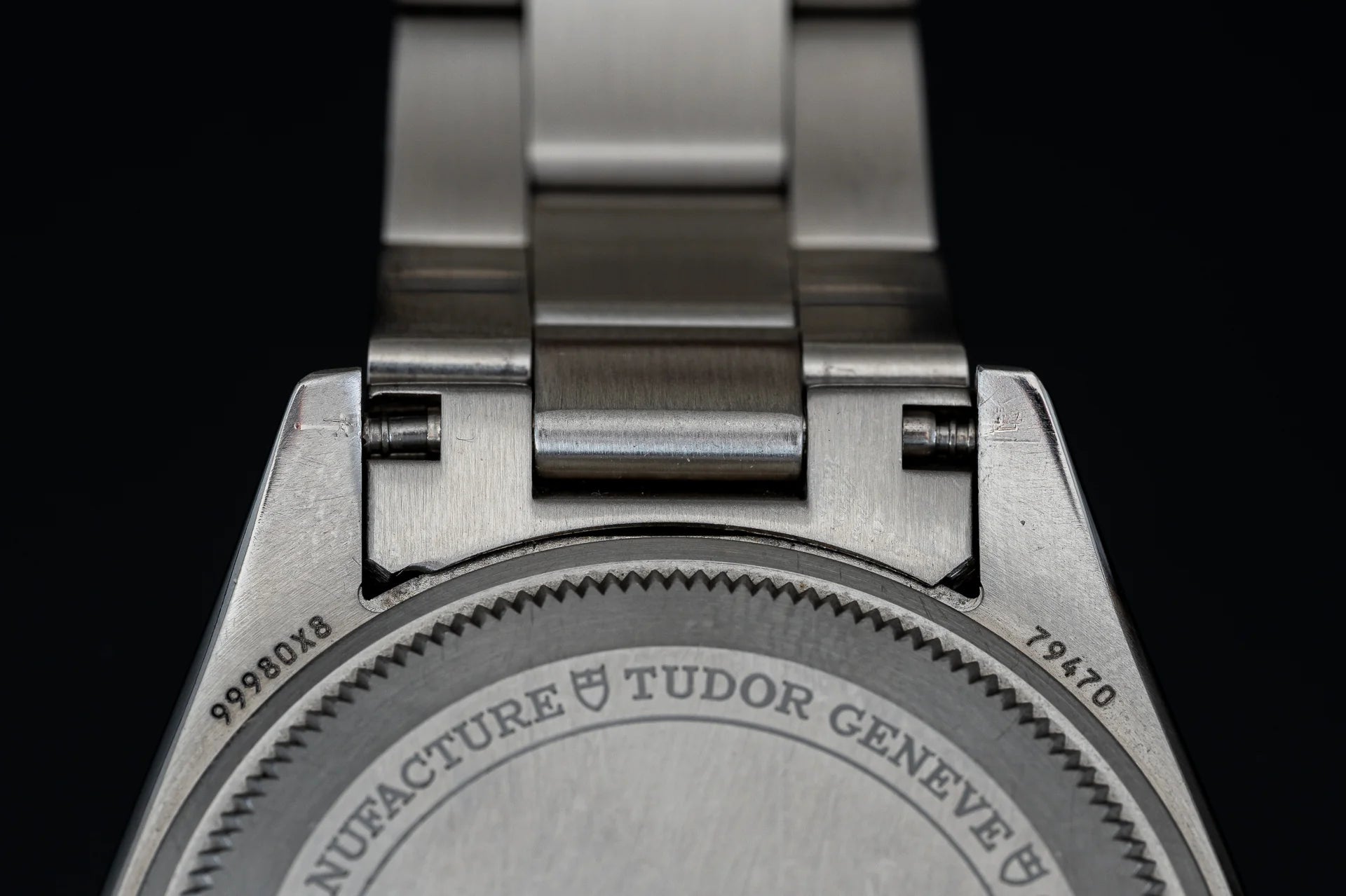 Stainless steel watch bracelet end link detail showing Tudor logo and manufacturing numbers on brushed metal surface