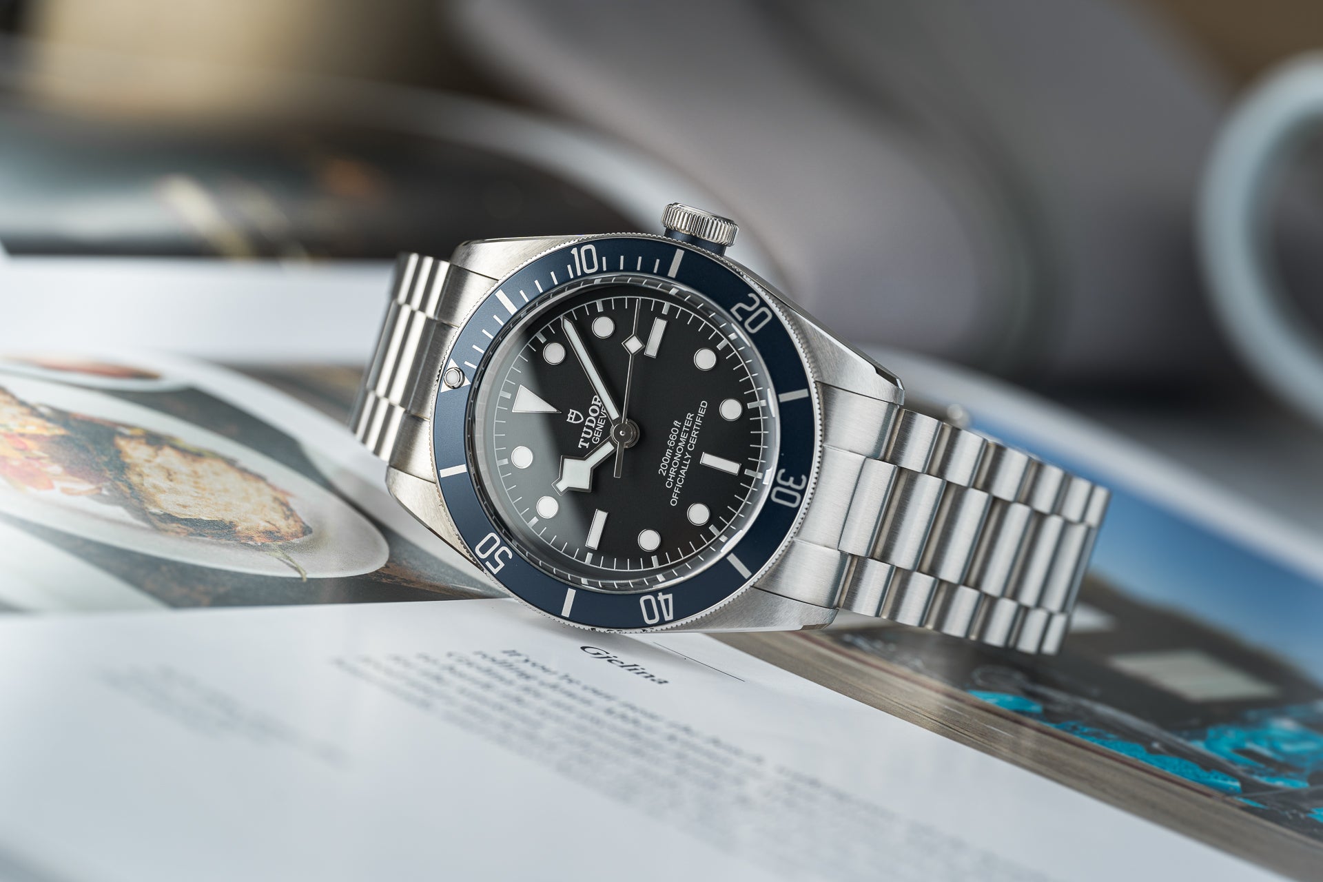 Tudor Black Bay 41mm dive watch with stainless steel bracelet on magazine, featuring black dial and blue bezel