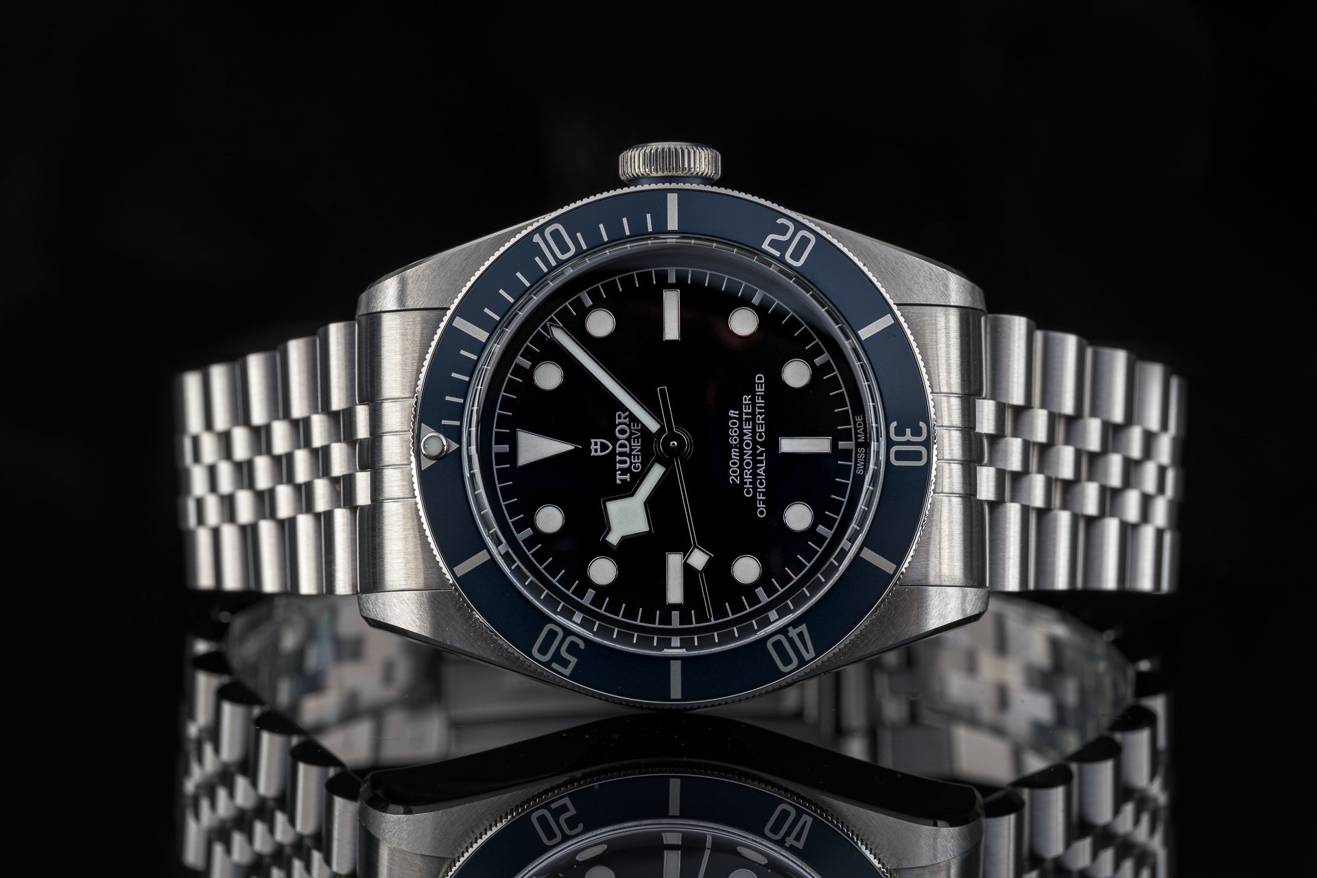 Tudor Black Bay stainless steel sports watch with blue bezel, black dial, and matching metal bracelet on black background