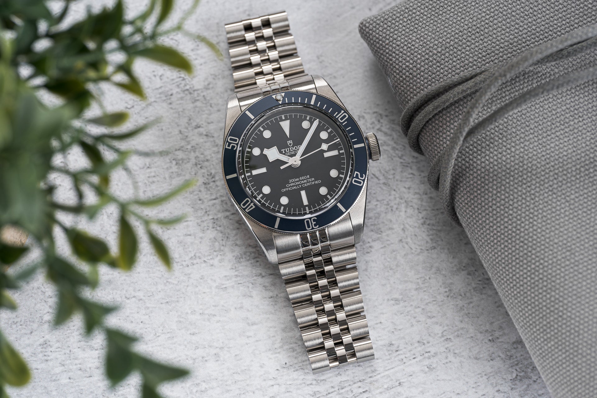 Tudor Black Bay stainless steel dive watch with black dial and bezel on jubilee bracelet next to gray fabric