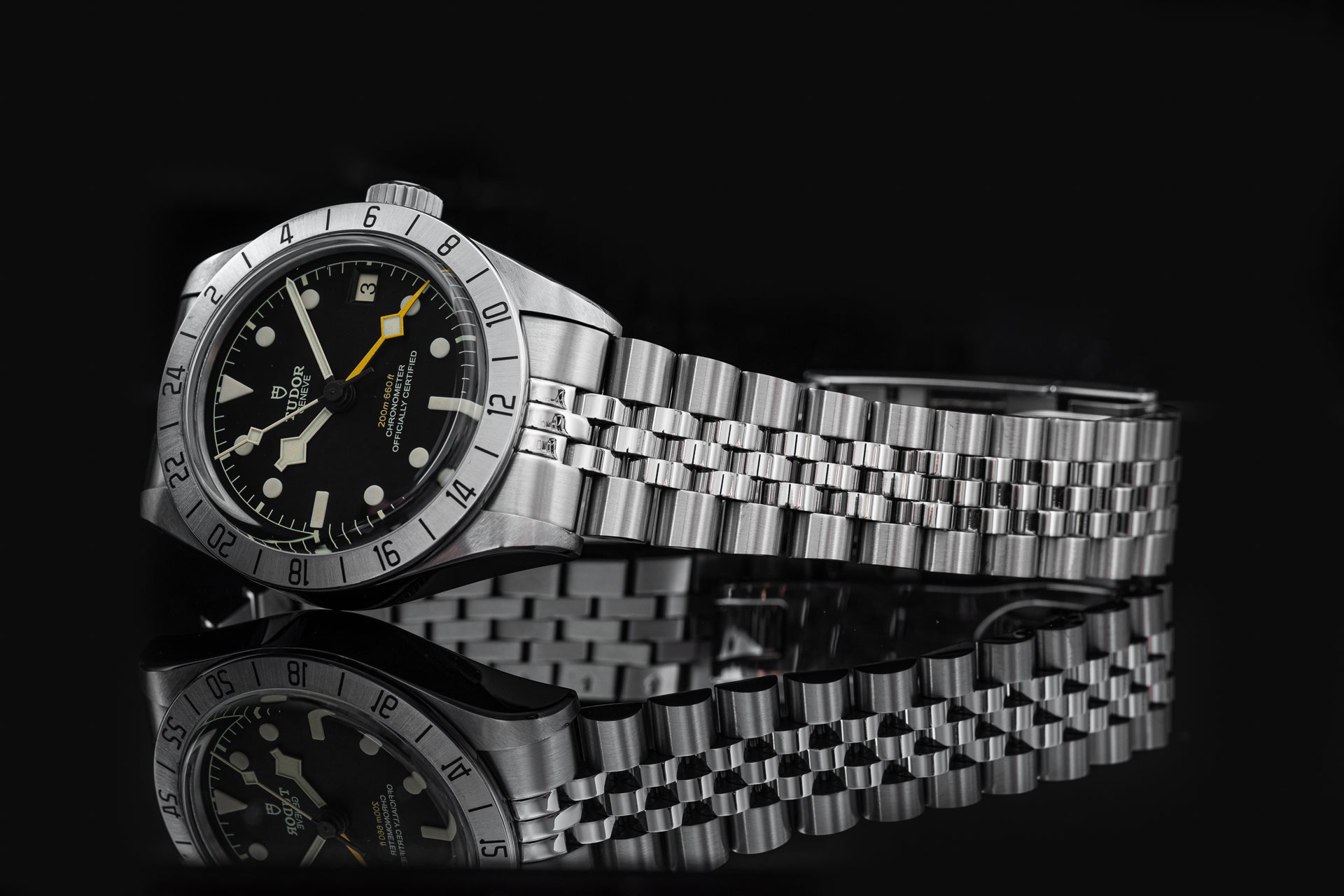 Stainless steel Tudor Black Bay Pro watch with black dial, gold hands, rotatable bezel, and jubilee bracelet on black background