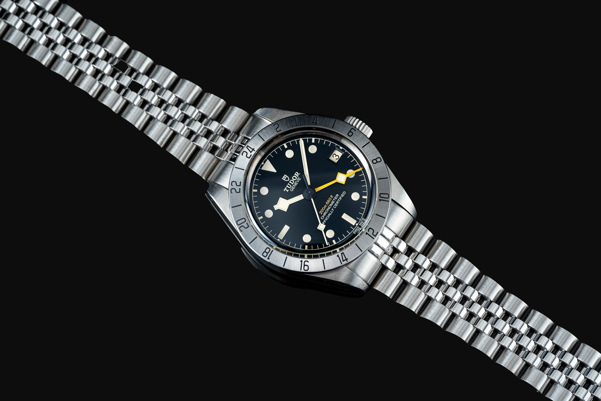Tudor Black Bay Pro dive watch with stainless steel bracelet, black dial, white hour markers, yellow GMT hand, and rotating bezel on black background