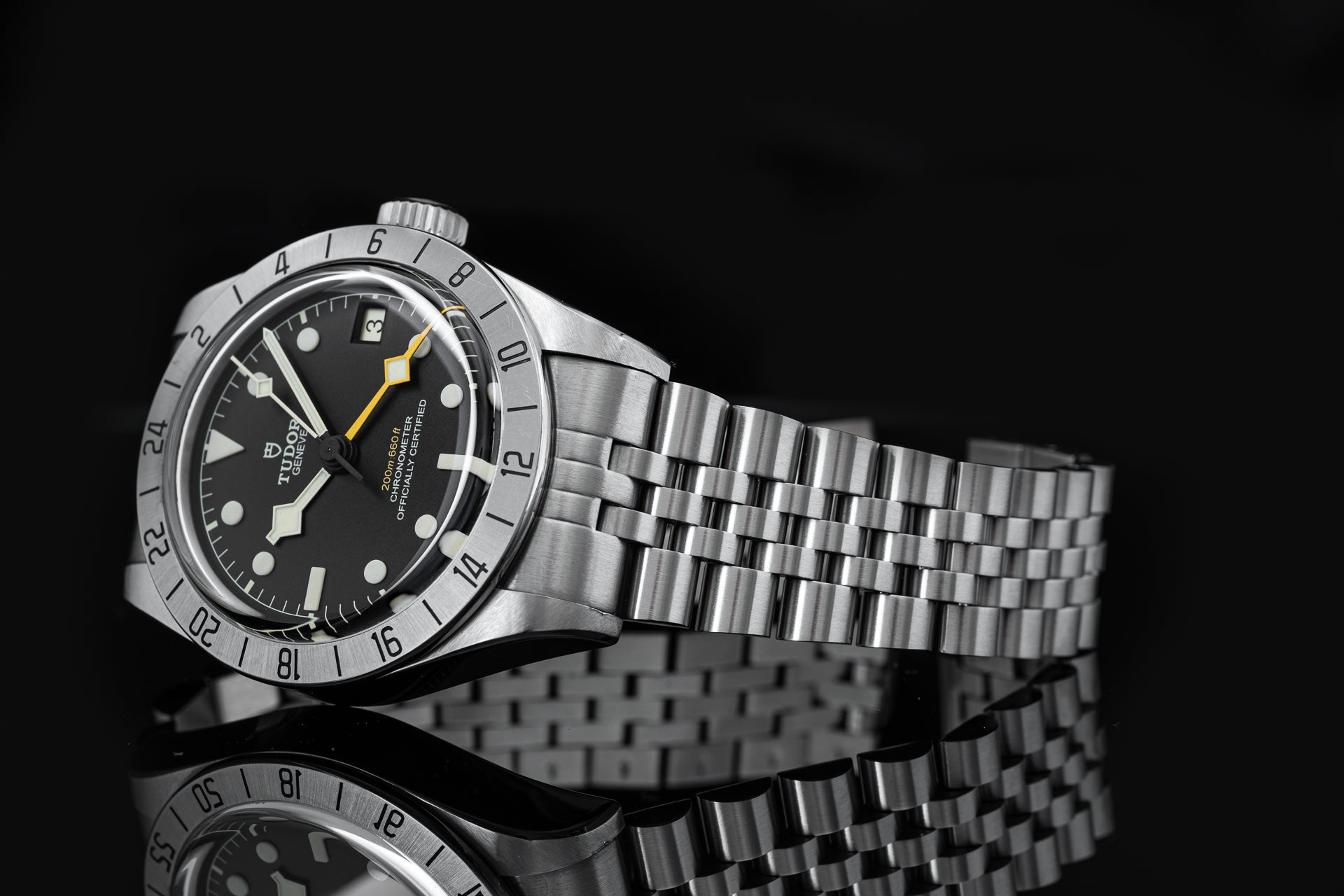 Stainless steel Tudor Black Bay Pro watch with black dial, yellow hands, numbered bezel, and matching metal bracelet on black background