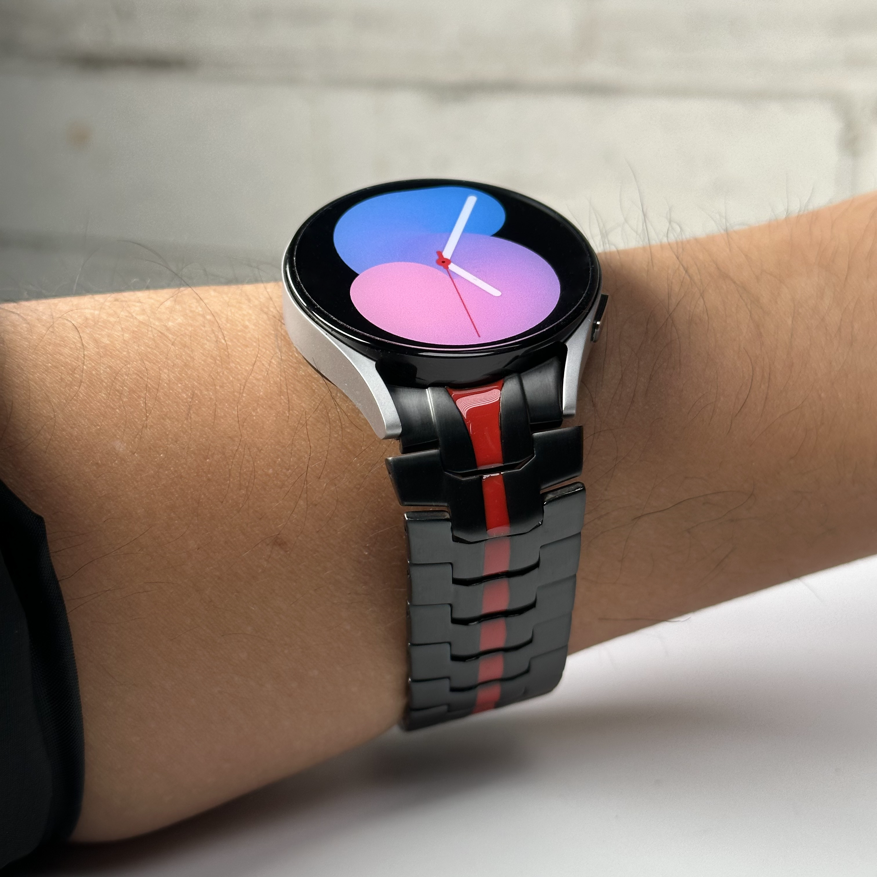 Smartwatch with black and red steel bracelet displaying gradient blue-to-pink watch face on wrist