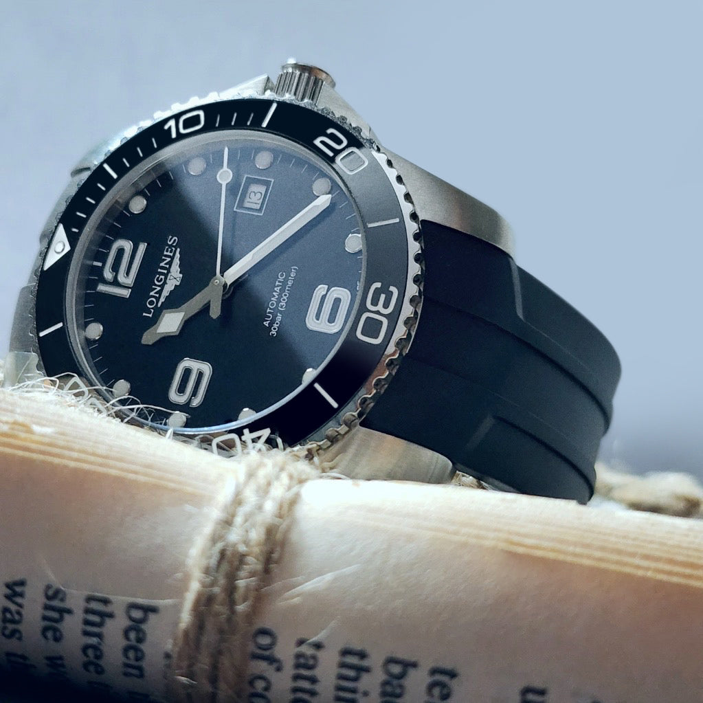 Longines Hydroconquest watch with black FKM rubber strap on rope background, showing stainless steel case and rotating bezel