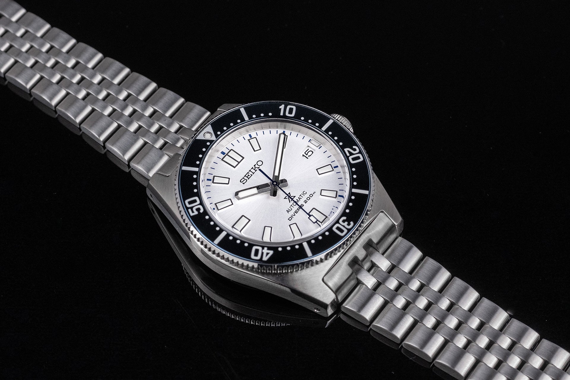 Seiko SPB143 62MAS reissue automatic diver watch with white dial, black bezel, and stainless steel bracelet on black background