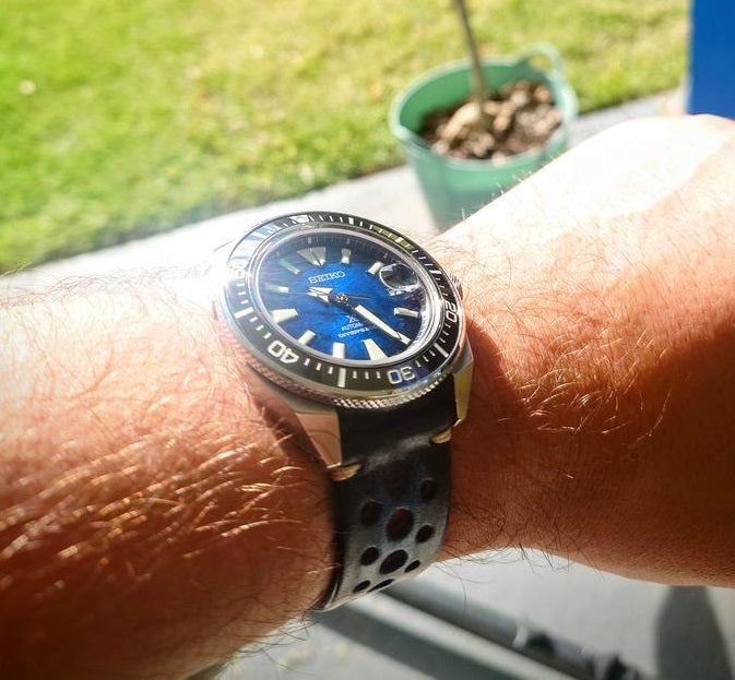 Seiko dive watch with blue dial and black bezel on smoked leather quick release rally strap worn on wrist outdoors