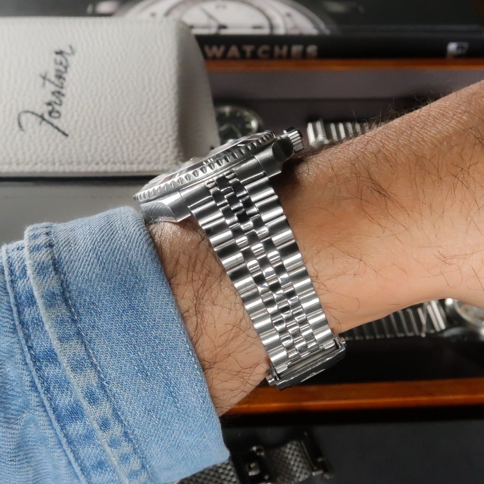 Silver stainless steel bracelet with jubilee links worn on wrist, showcasing integrated end links and polished finish against watch box packaging