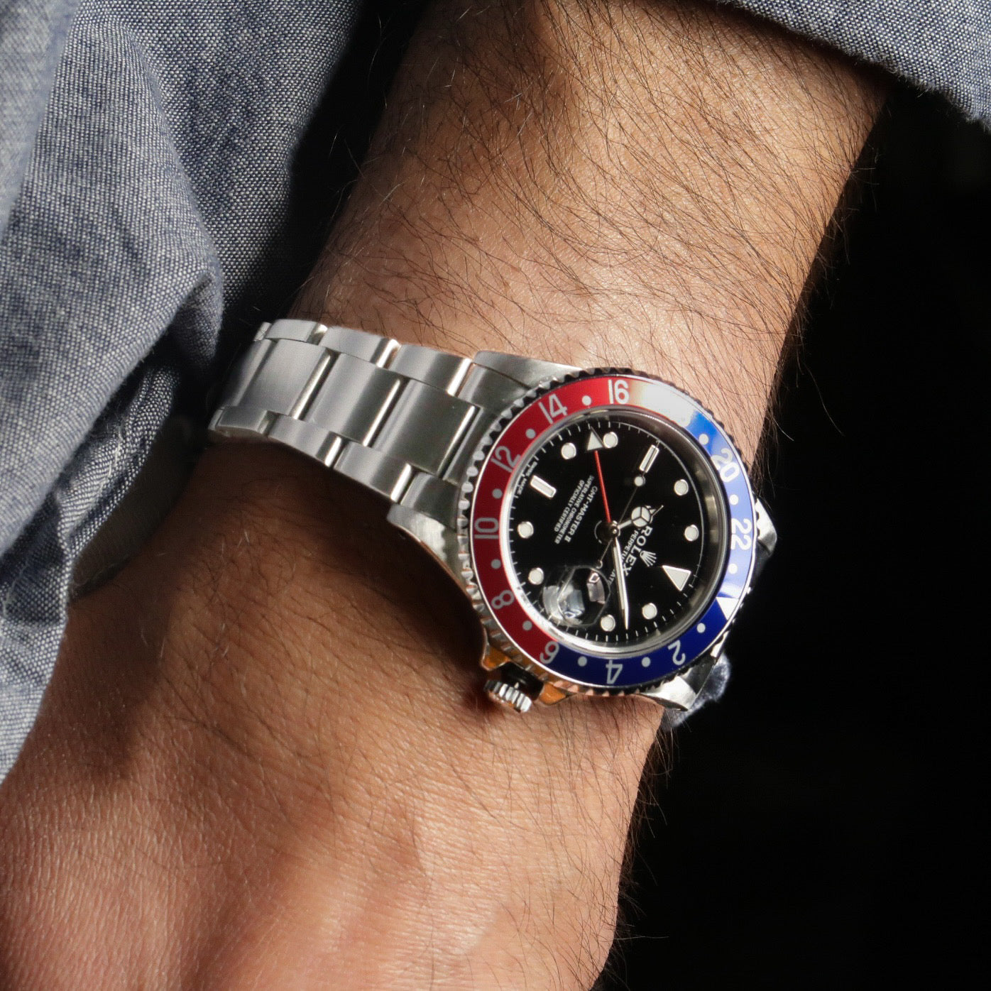 Stainless steel dive watch with red and blue GMT bezel on wrist, black dial with white markers and metal bracelet
