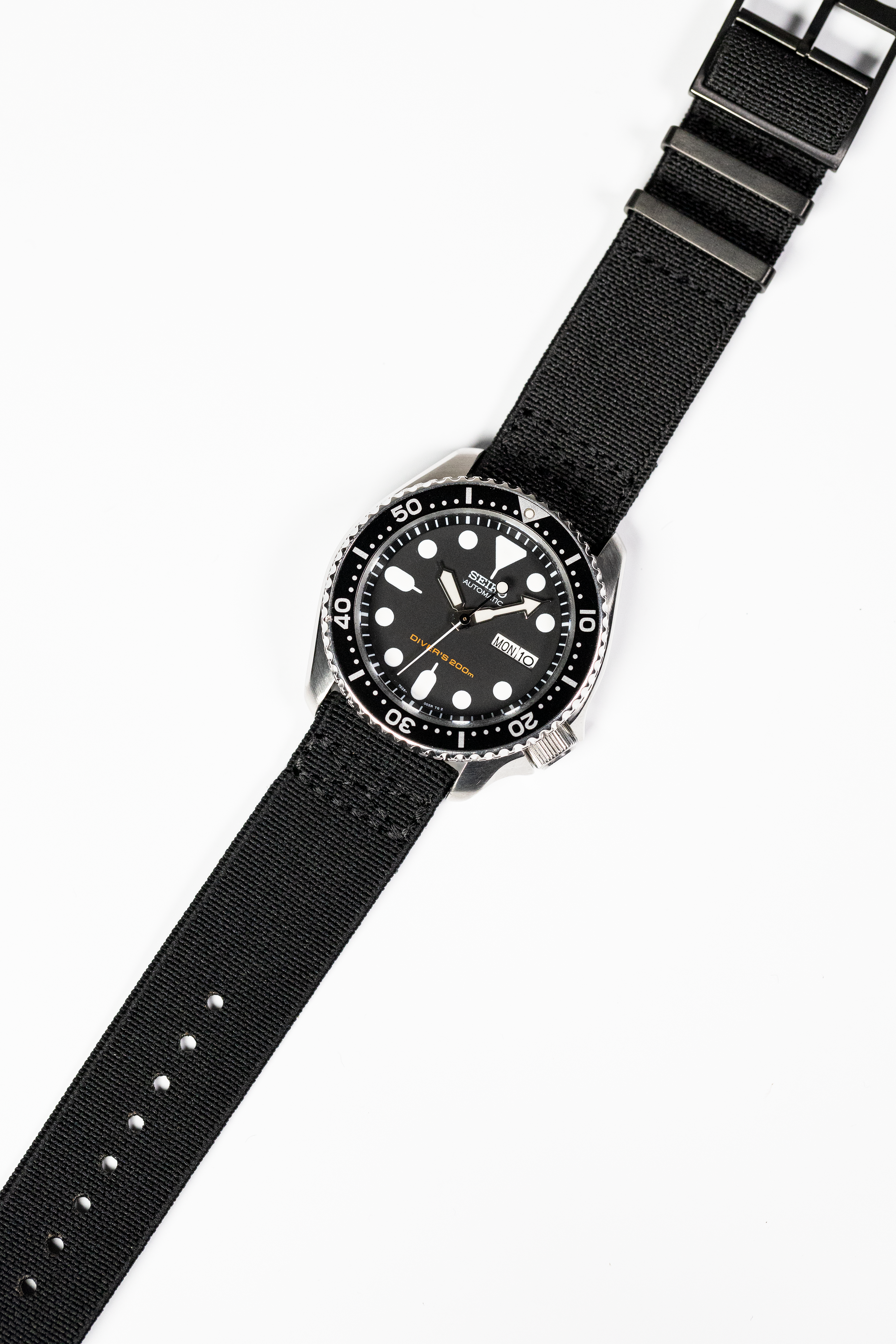 Black dive watch with stainless steel case, black dial, white dot indices, rotating bezel, and black fabric strap with metal hardware