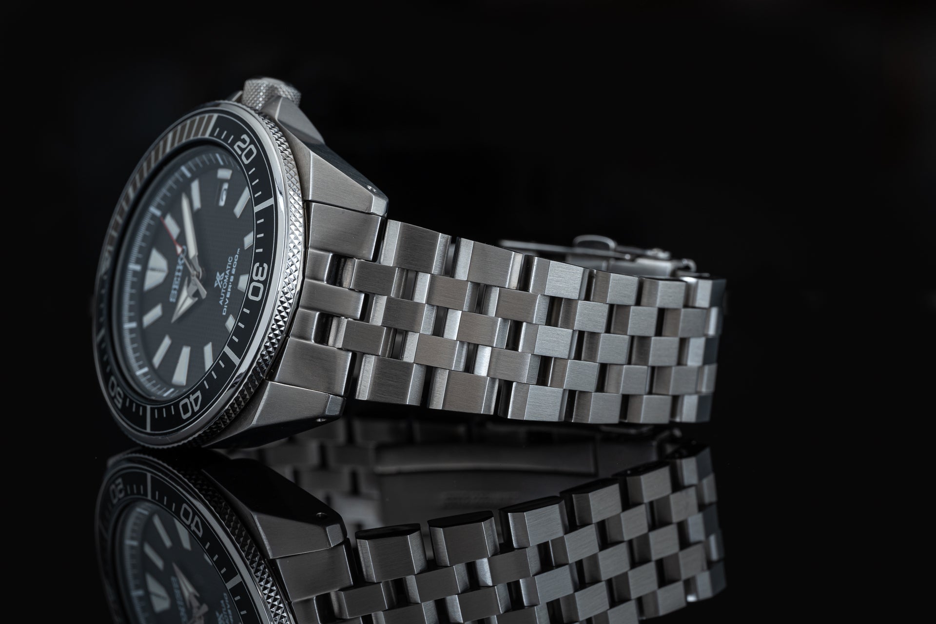 Stainless steel diving watch with black dial, rotating bezel, and matching metal bracelet displayed on black background