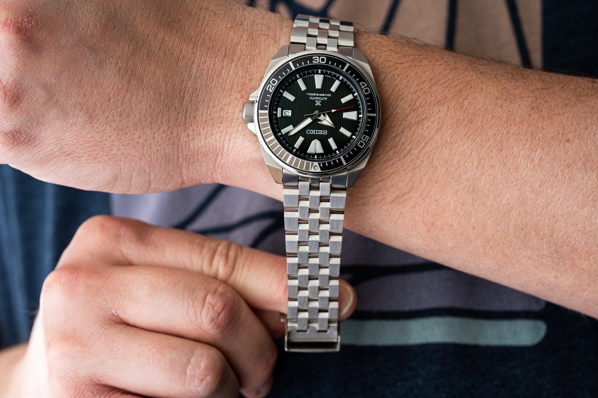 Stainless steel dive watch with black dial and date window worn on metal bracelet on wrist
