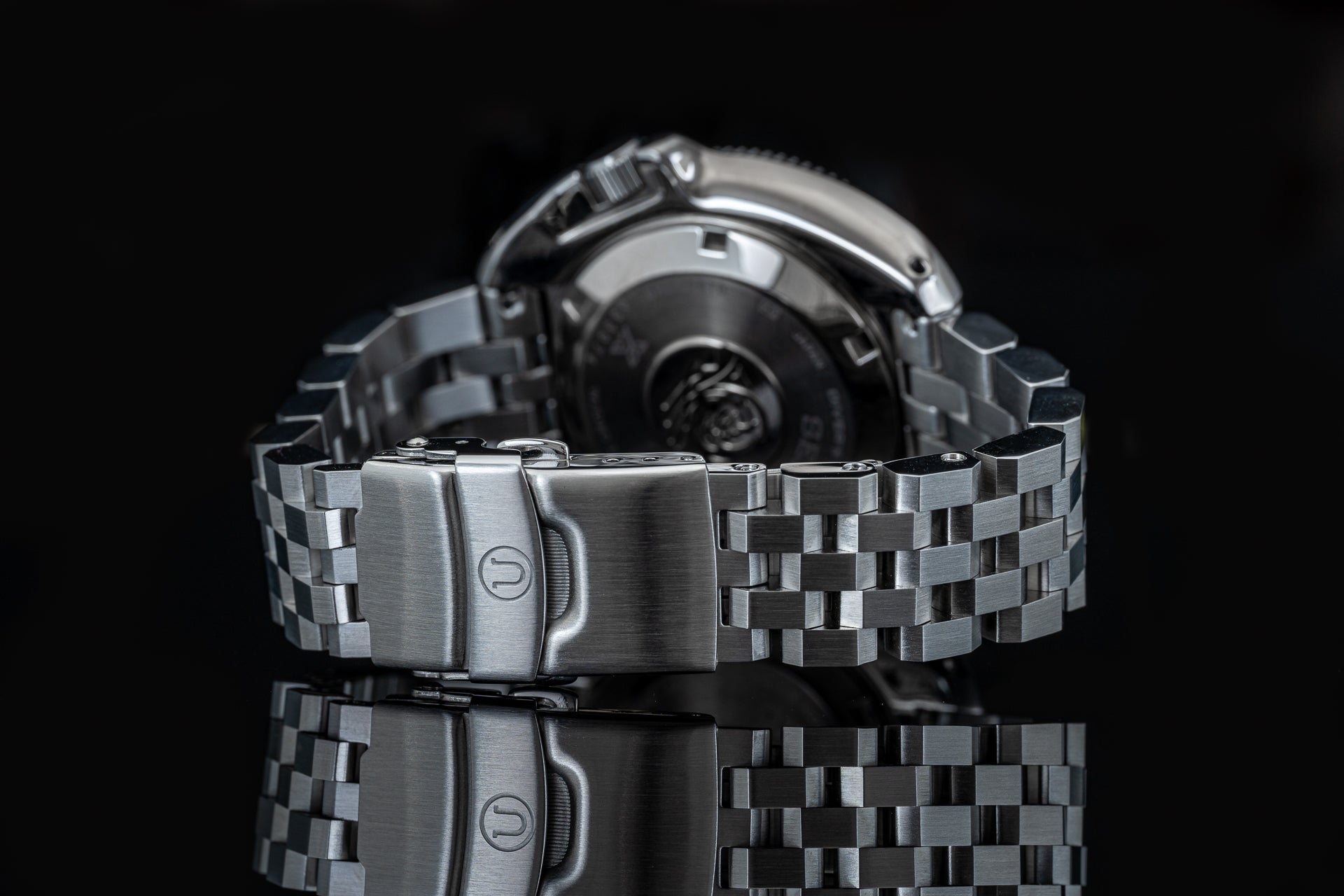 Stainless steel watch bracelet with solid link construction and fold-over clasp, front view against black background