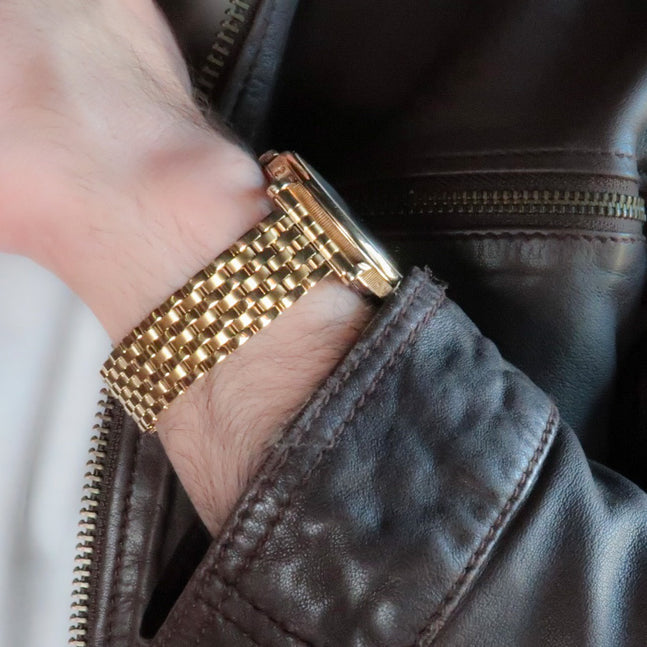 Gold plated beads of rice watch bracelet with 7-row mesh design worn on wrist with black leather jacket